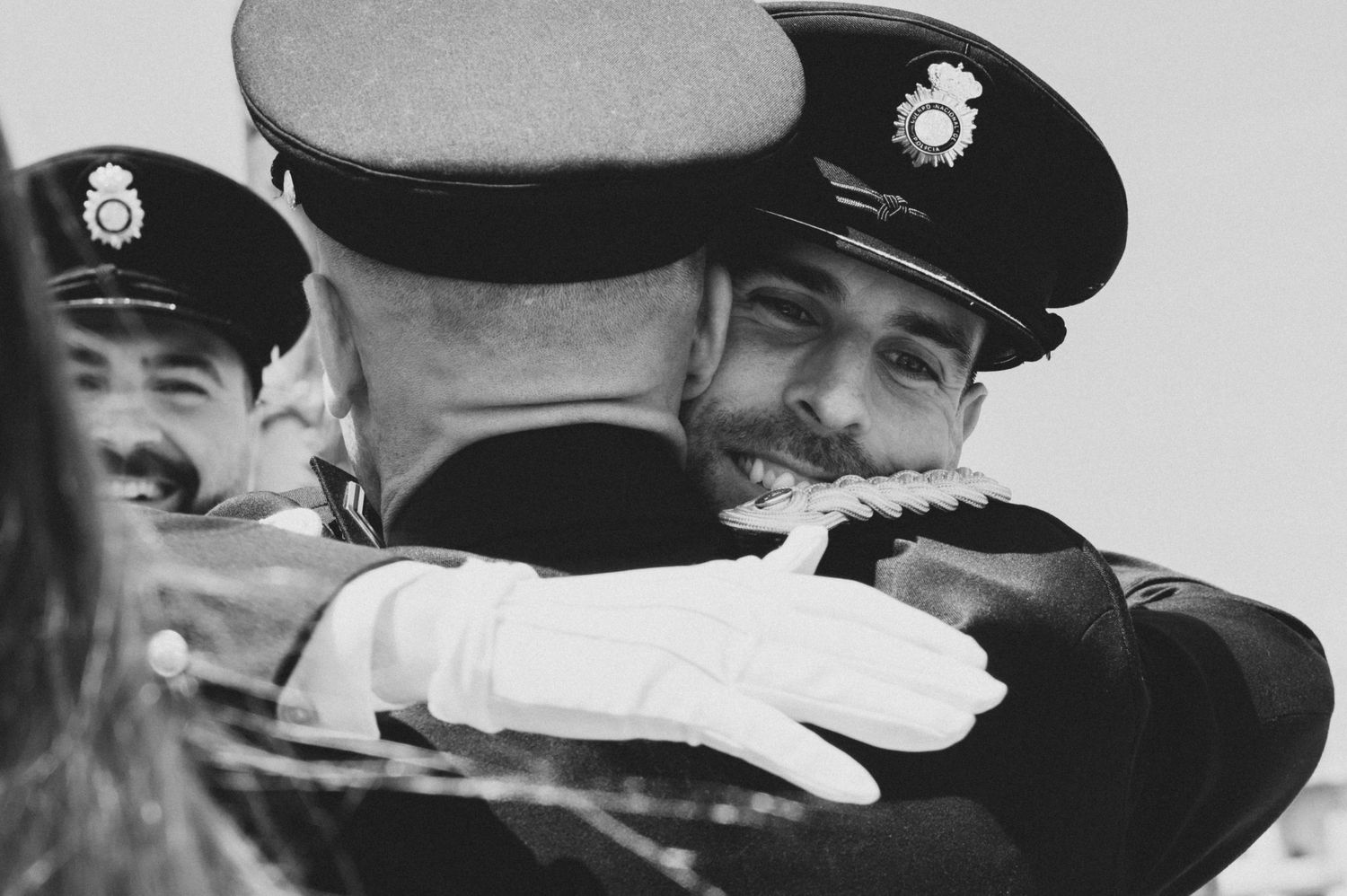 Military officers in dress uniforms and caps embracing at formal ceremony.