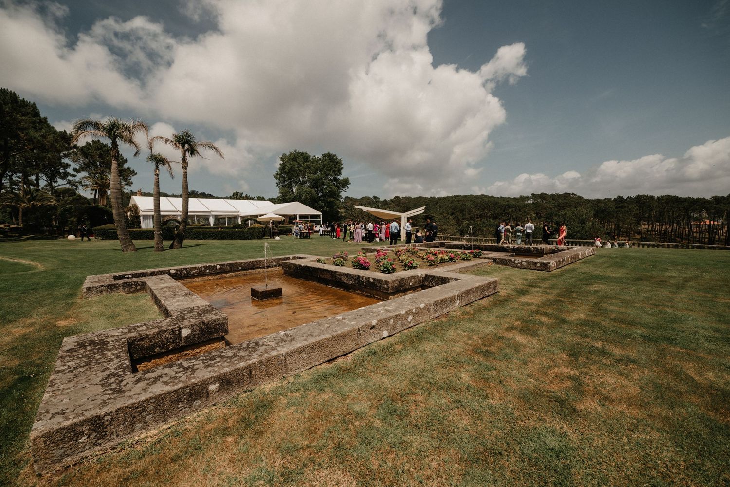 Panoramic view of an archaeological excavation site with stone foundations and grassy terrain under cloudy skies.