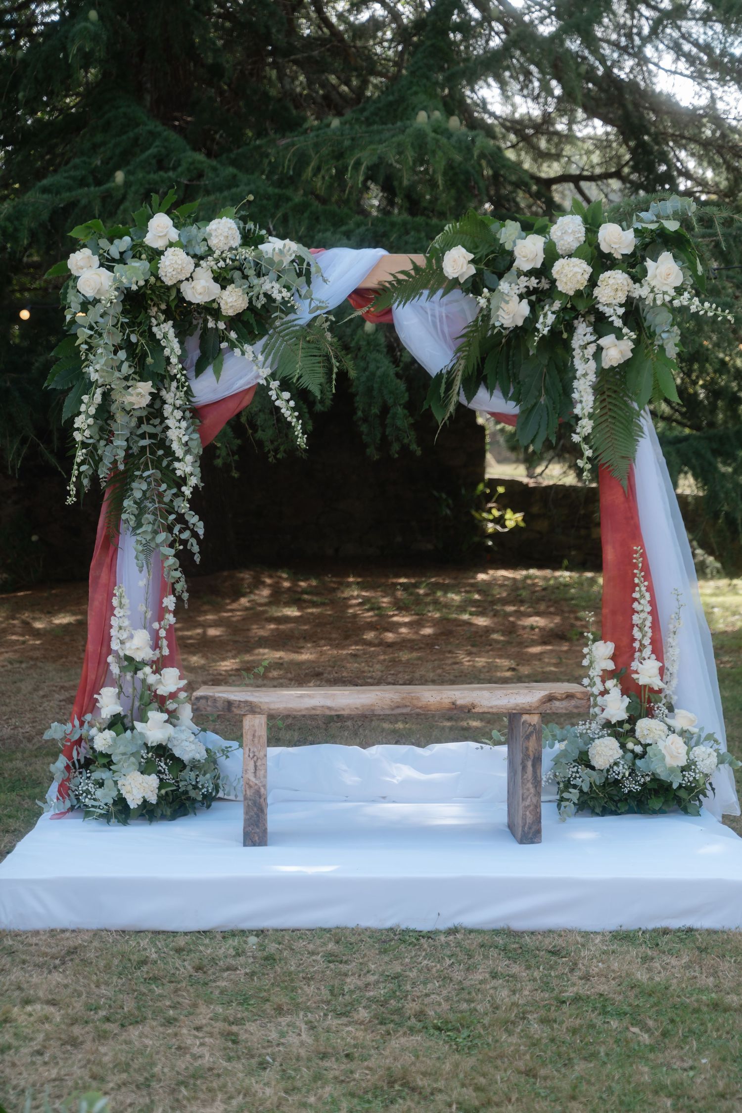 Wedding arch decorated with white flowers and draped fabric stands elegantly on a grassy lawn at an outdoor venue.