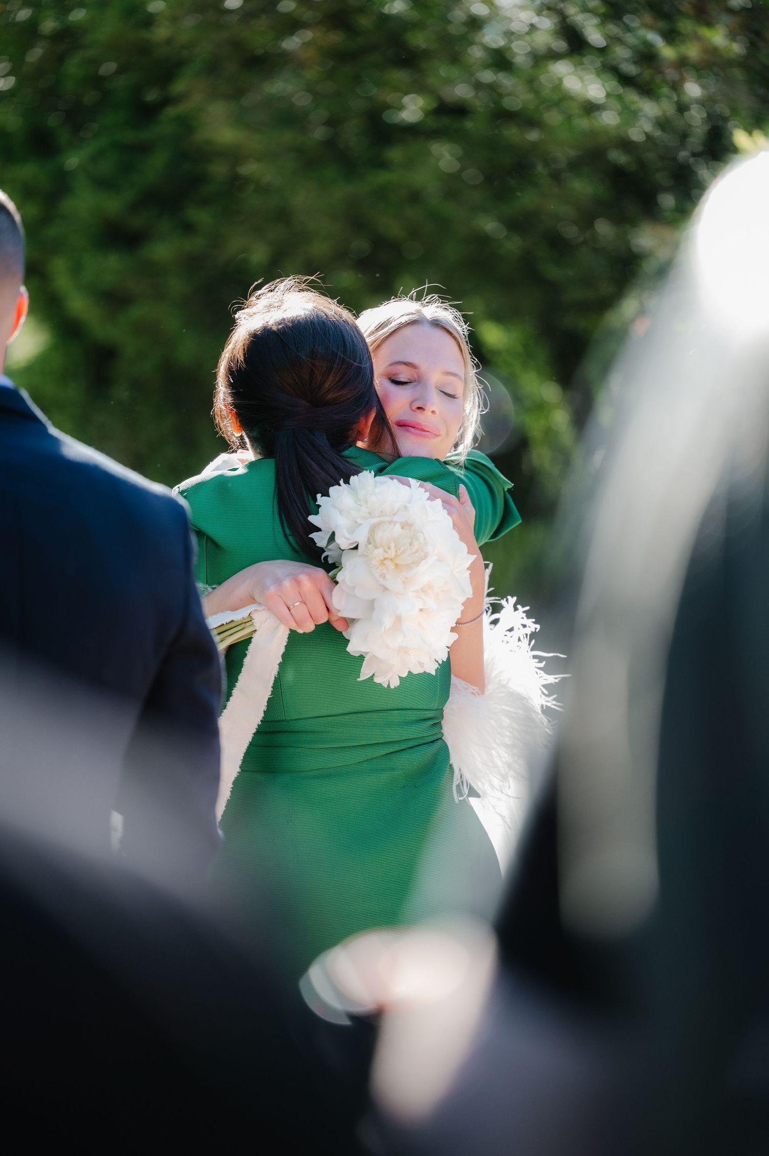 Wedding party members in green dresses hold white bouquets during an outdoor celebration.