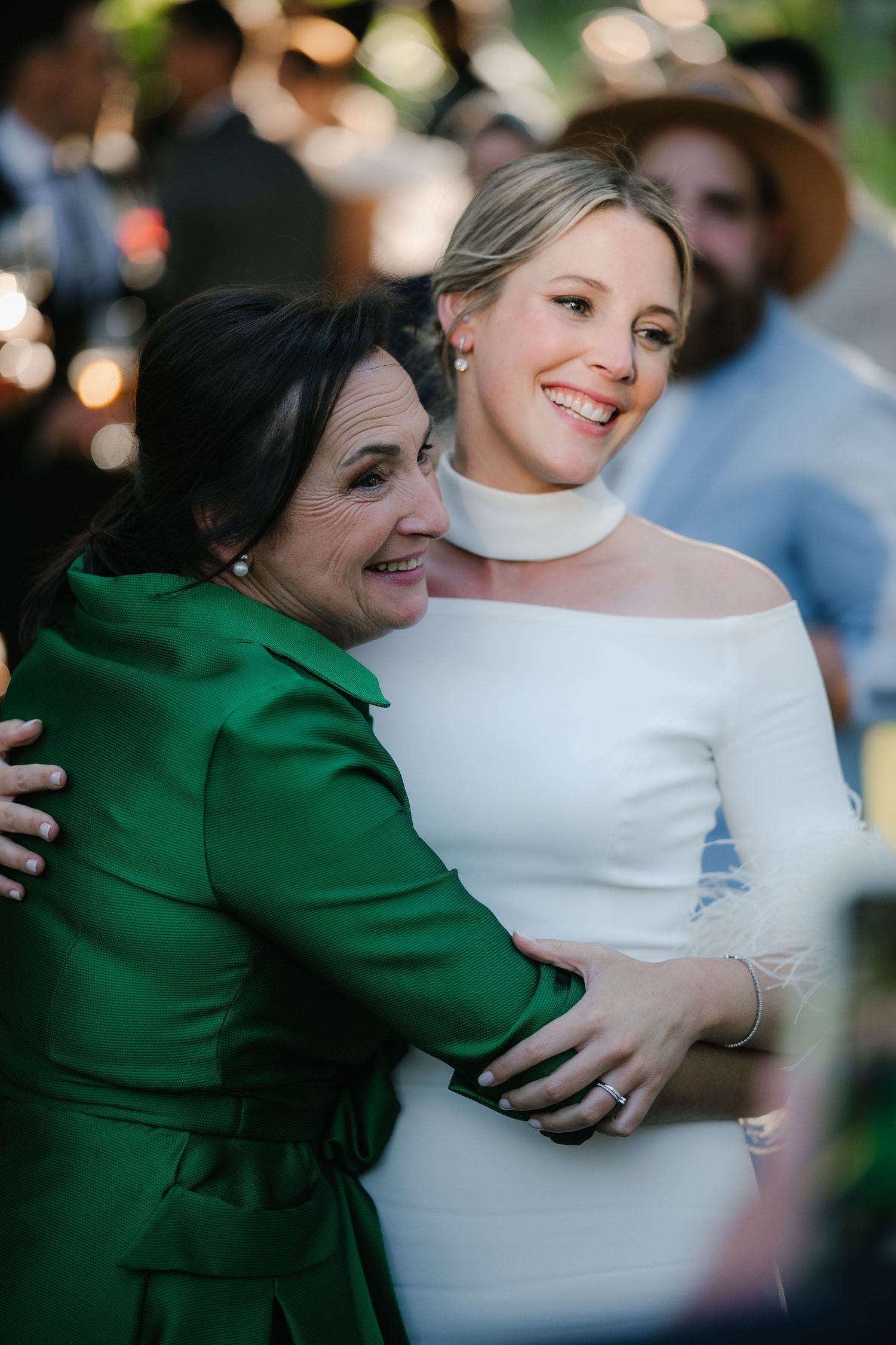 A heartfelt embrace between two wedding guests, one wearing an emerald green dress.