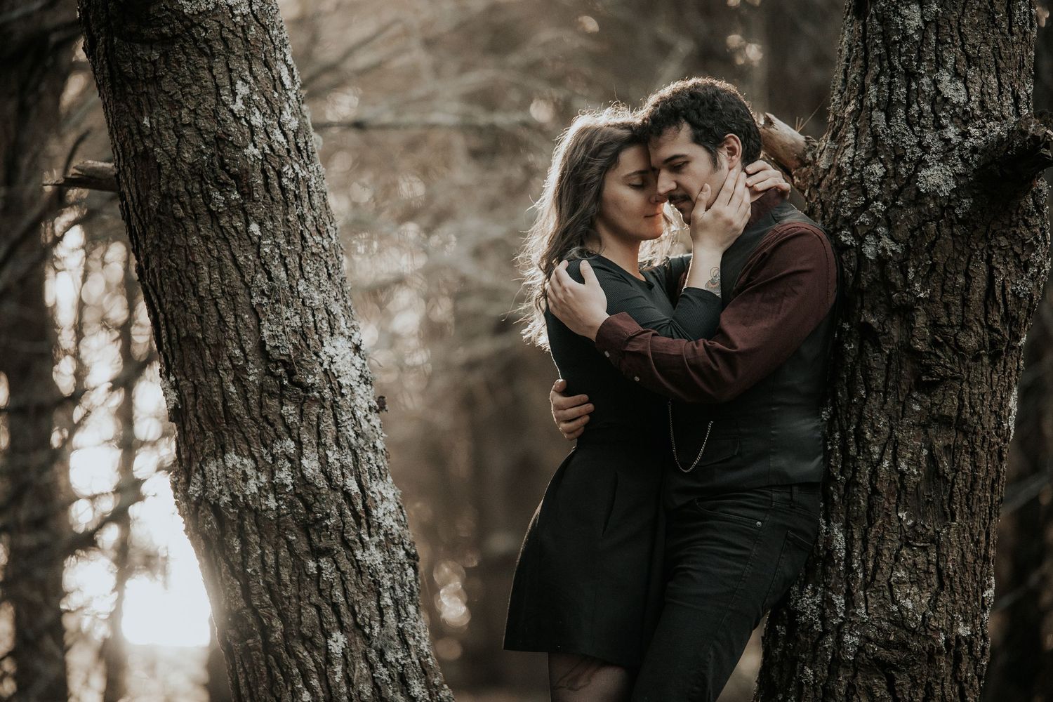 Two people embrace against a tree trunk in a dark wooded setting.