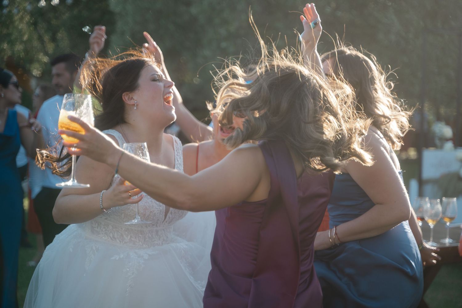 People dancing joyfully at an outdoor wedding reception with sunlight creating a magical backlit effect.