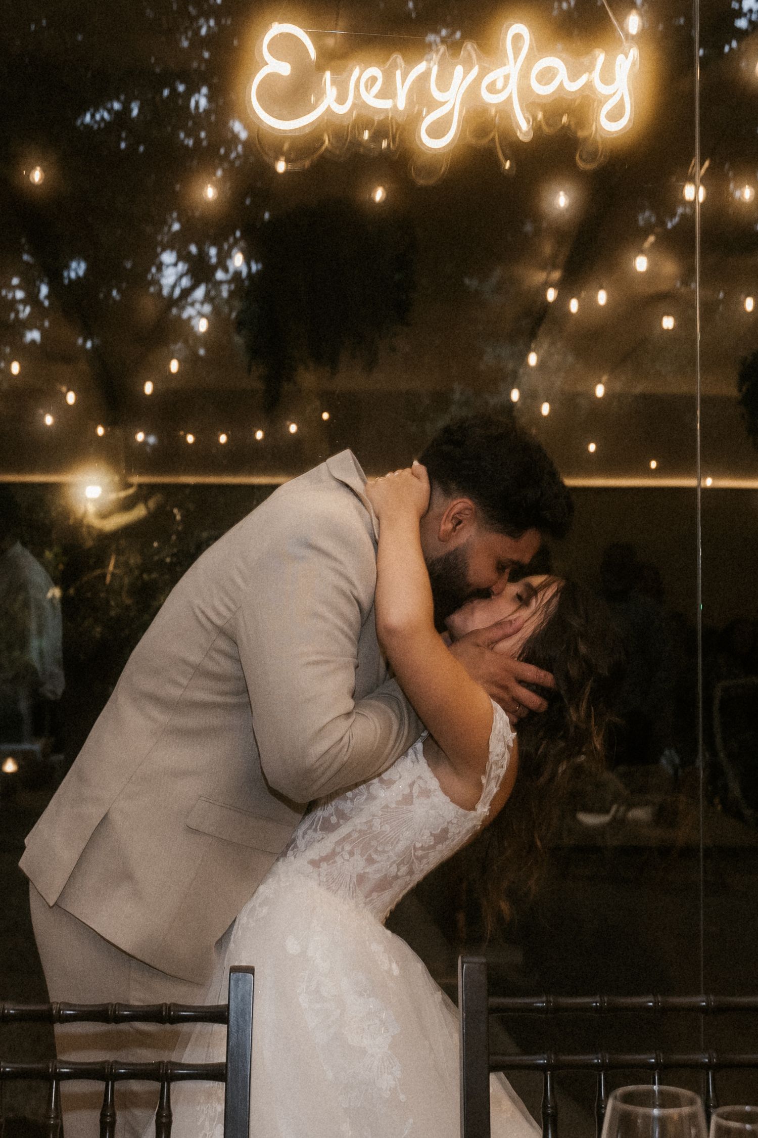 A romantic wedding kiss moment under glowing string lights at an evening reception.
