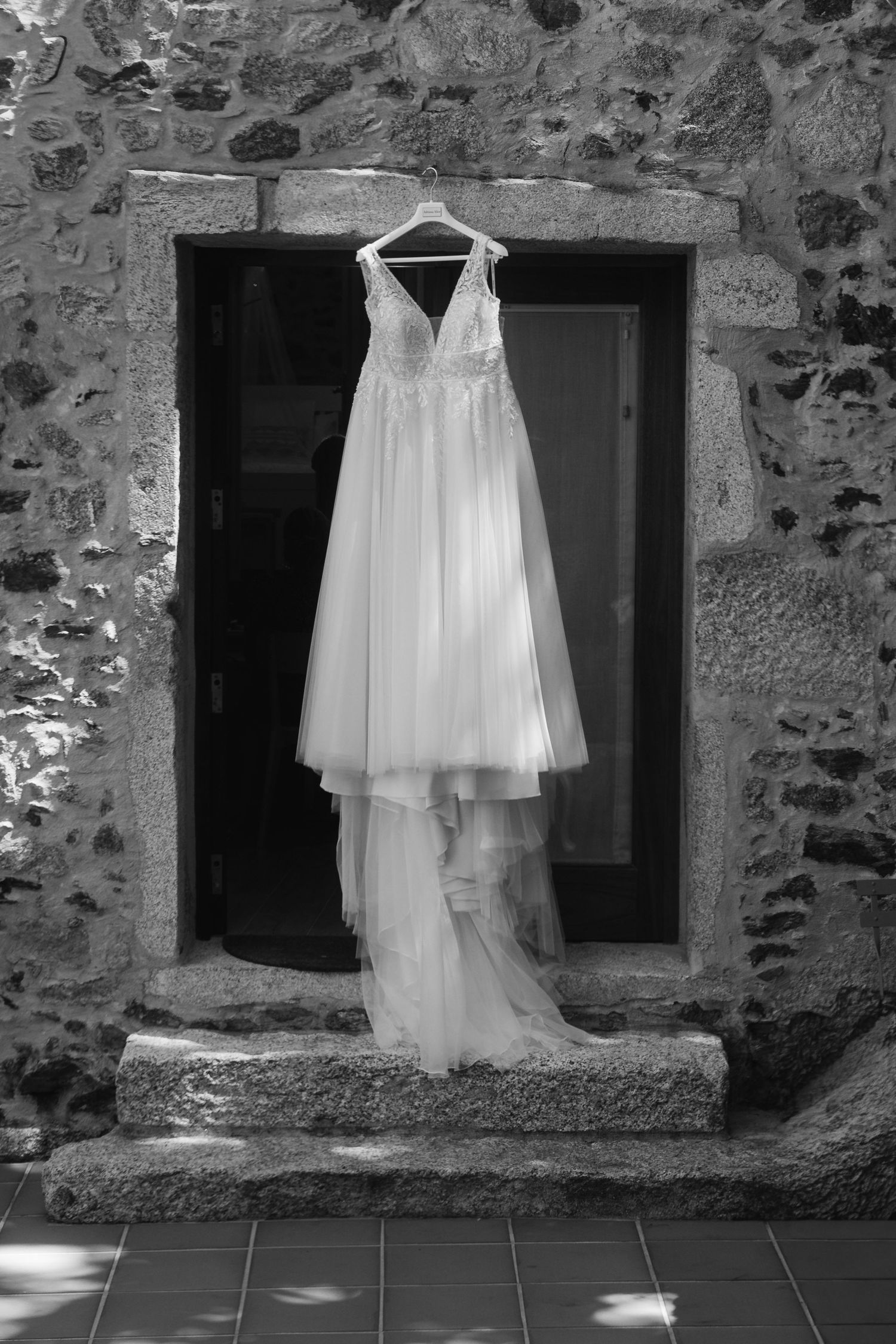 White wedding dress displayed on stone wall with rustic windows creating an ethereal bridal scene.