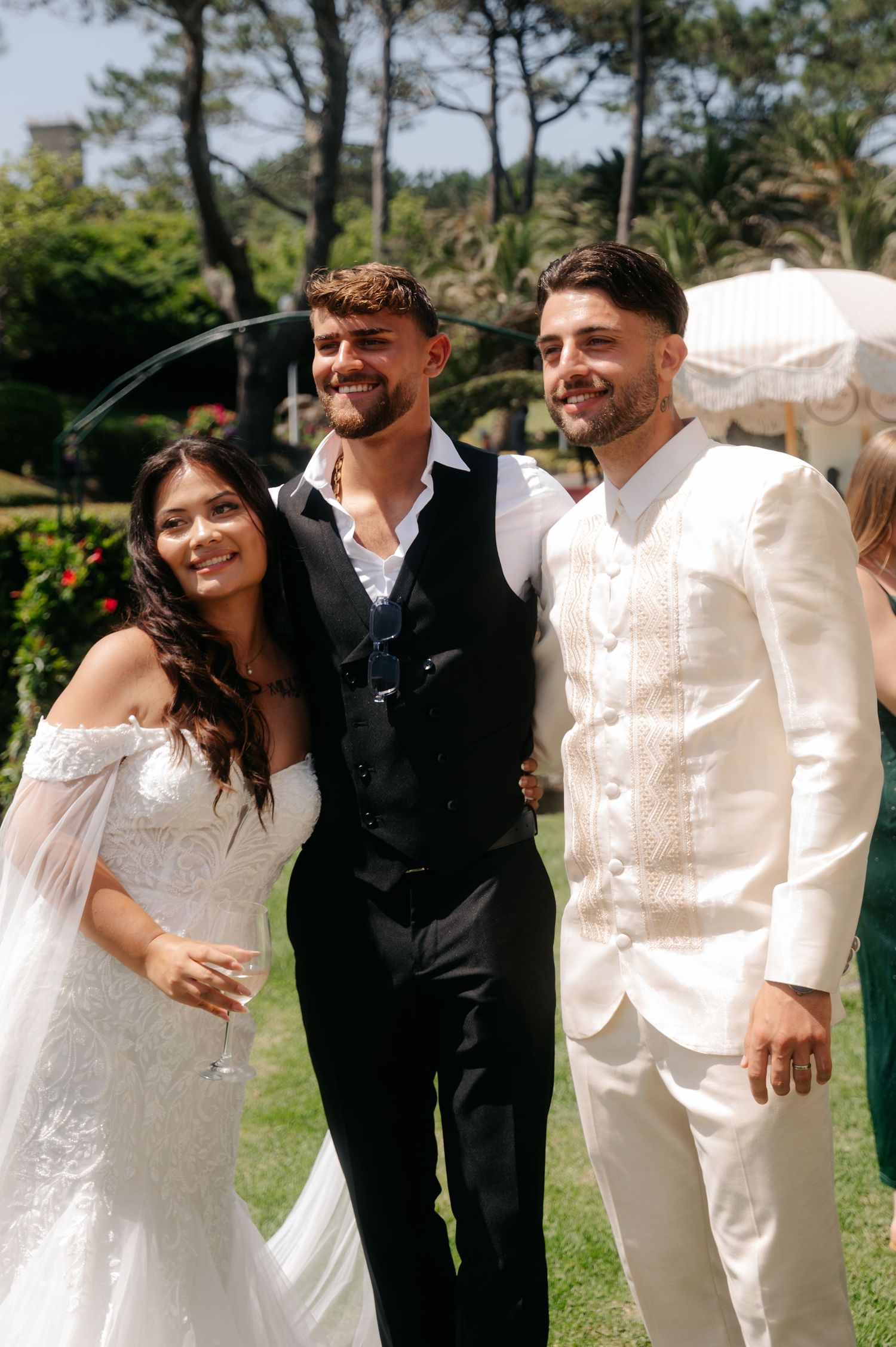 A wedding party poses together outdoors in black and white formal attire on a sunny day.