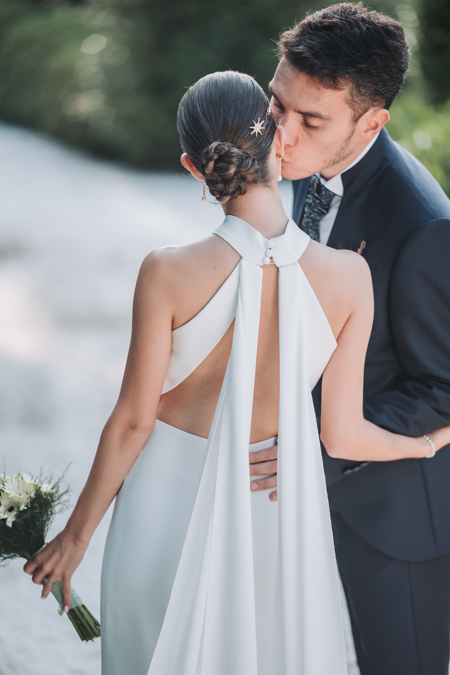 Close-up details of a bride's elegant halter wedding dress with white fabric and open back design.