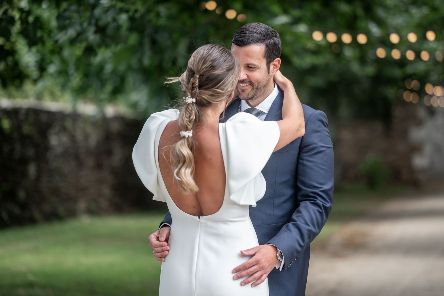 Bride and groom embrace during their first dance at an outdoor wedding reception with garden scenery.