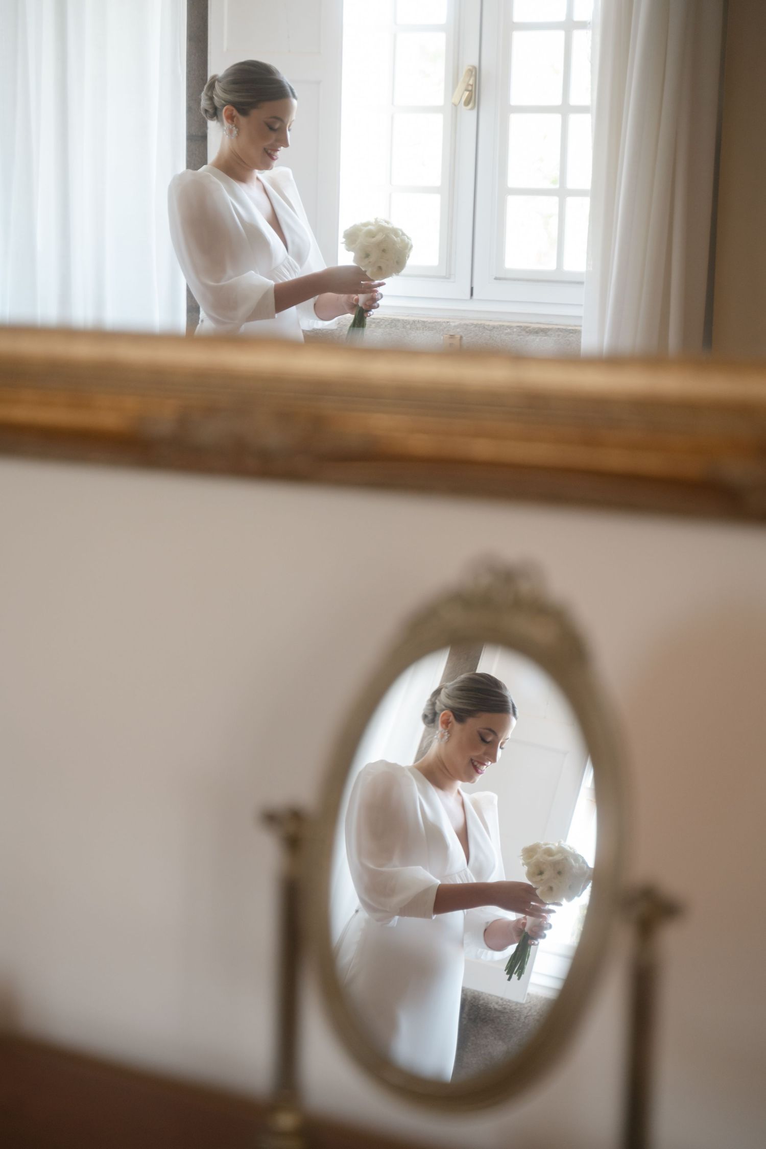 Wedding dress details reflected in vintage mirror with delicate white bouquet.