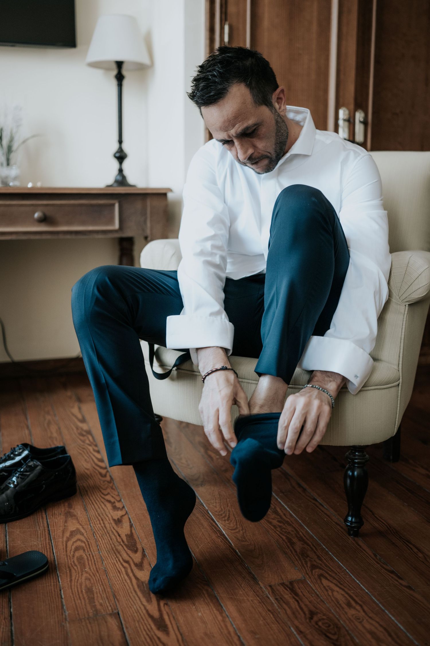 A sequence of photos showing someone sitting in a white chair putting on dark dress shoes with wooden flooring.