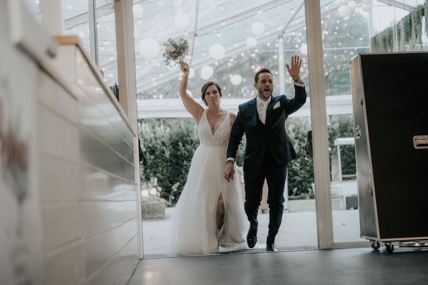 A joyful couple celebrates during their wedding reception entrance at a bright indoor venue.