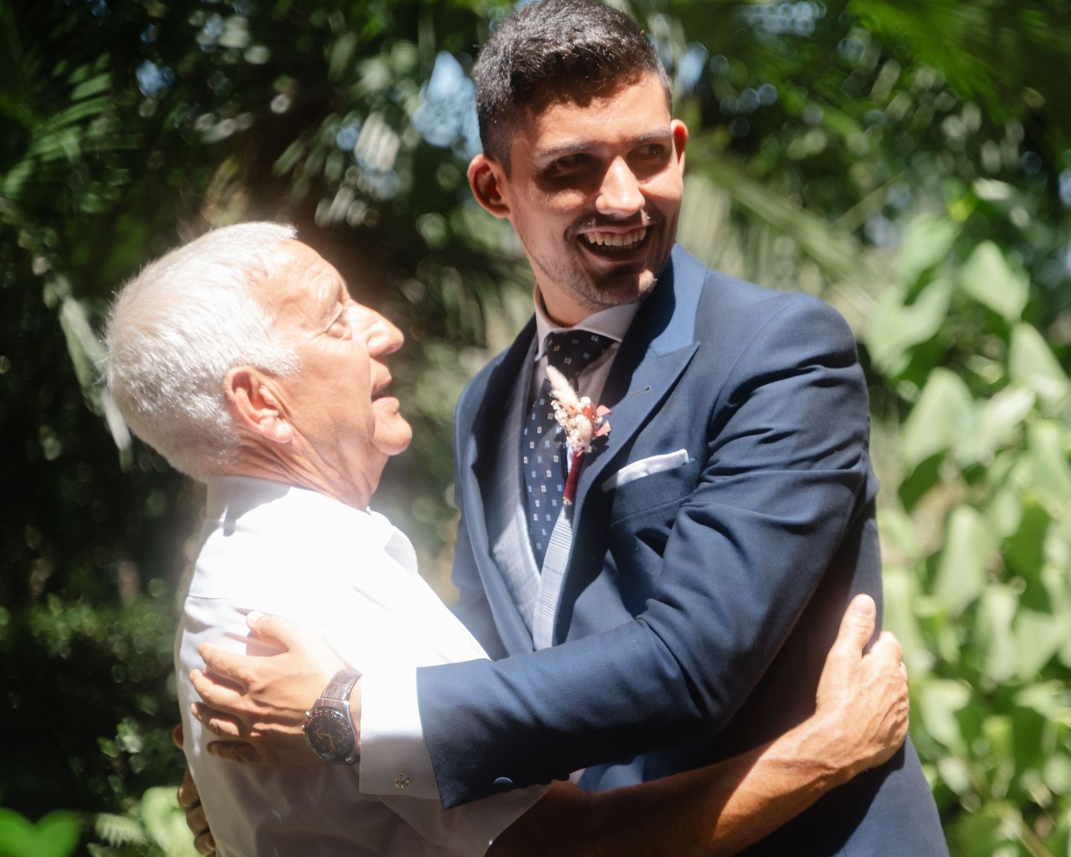 Emotional embrace captured during outdoor wedding ceremony with natural greenery backdrop.