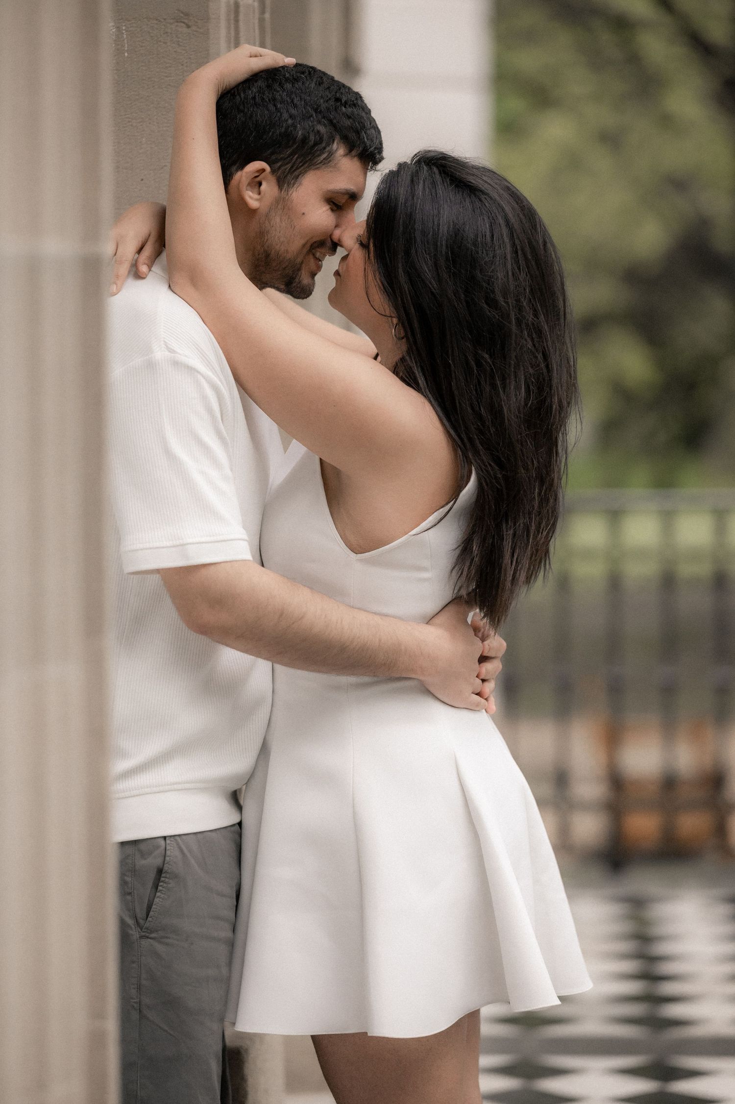 Romantic couple in white clothing embracing in an elegant columned setting.