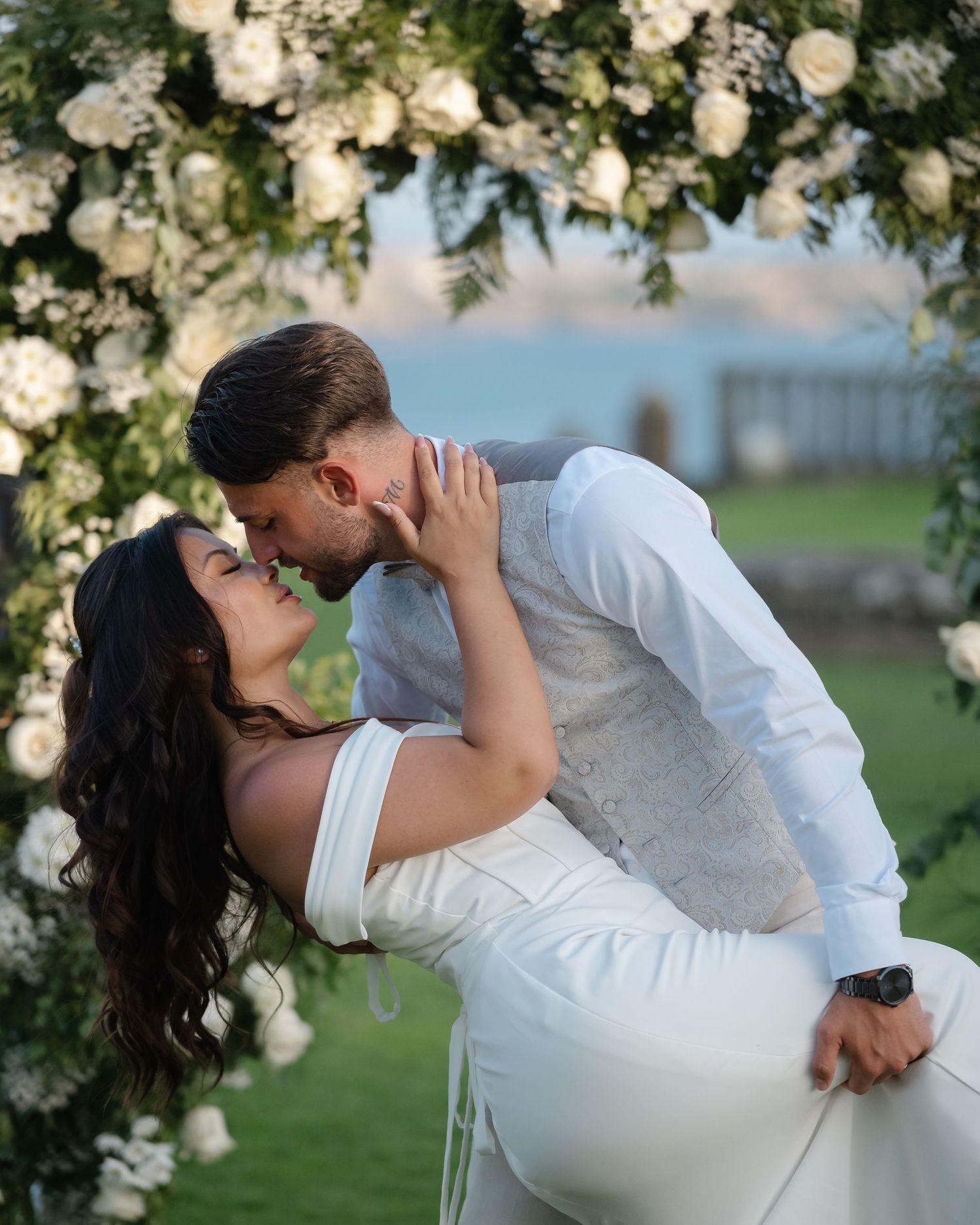 A romantic dip kiss between newlyweds under an arch of white roses.Wedding photographer Spain. Galicia.