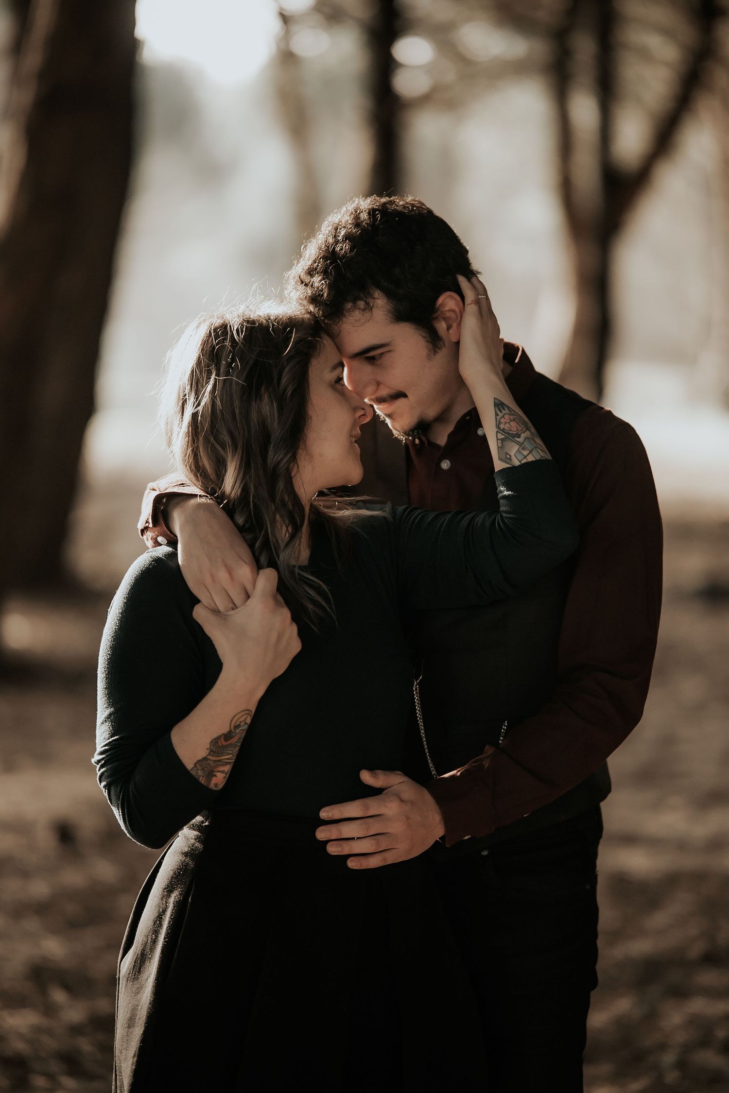 Romantic couple embraces intimately in moody forest setting with soft natural lighting and bokeh effect.