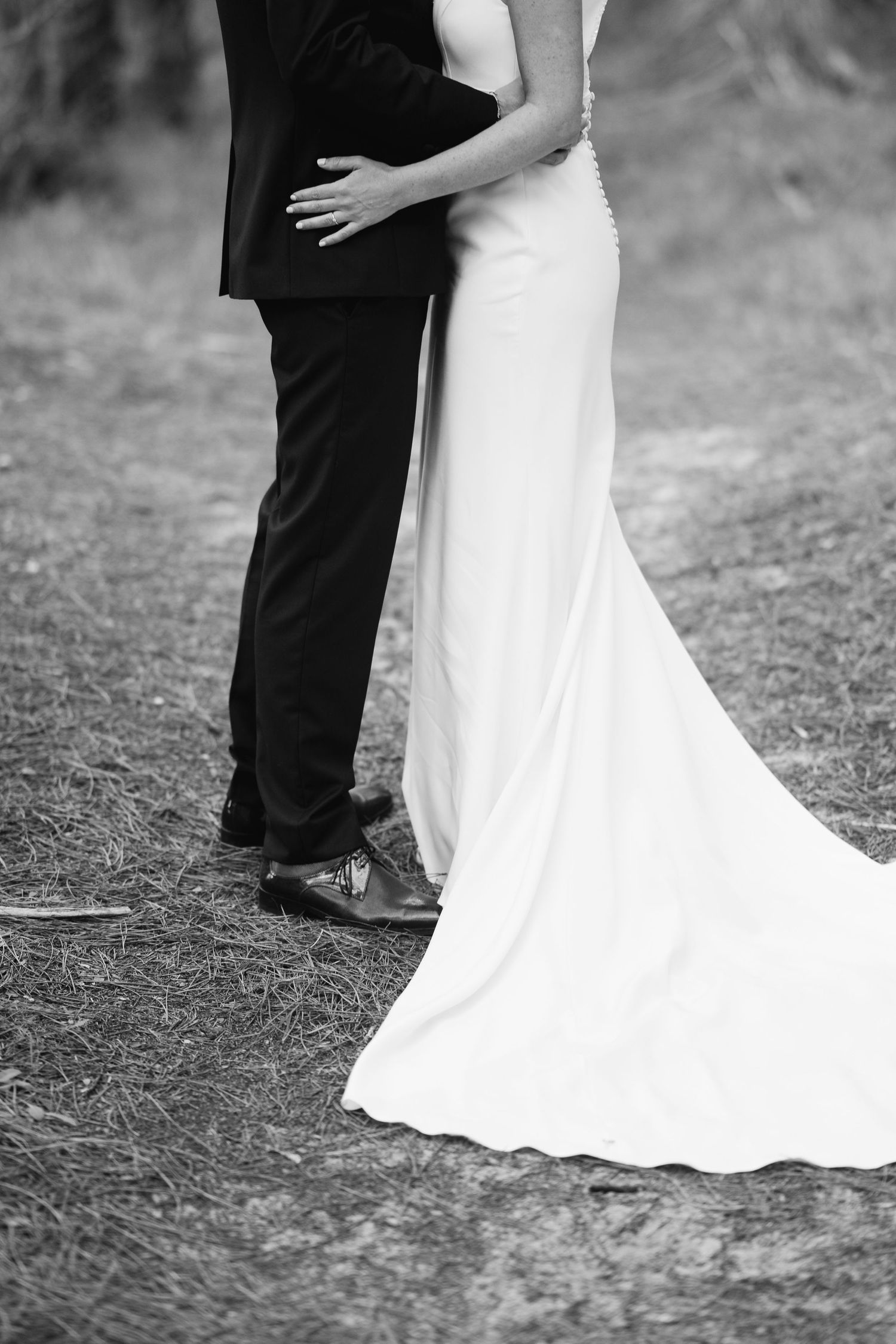 A black and white wedding photo showing the elegant silhouette of a bride's flowing dress against a groom's dark suit.