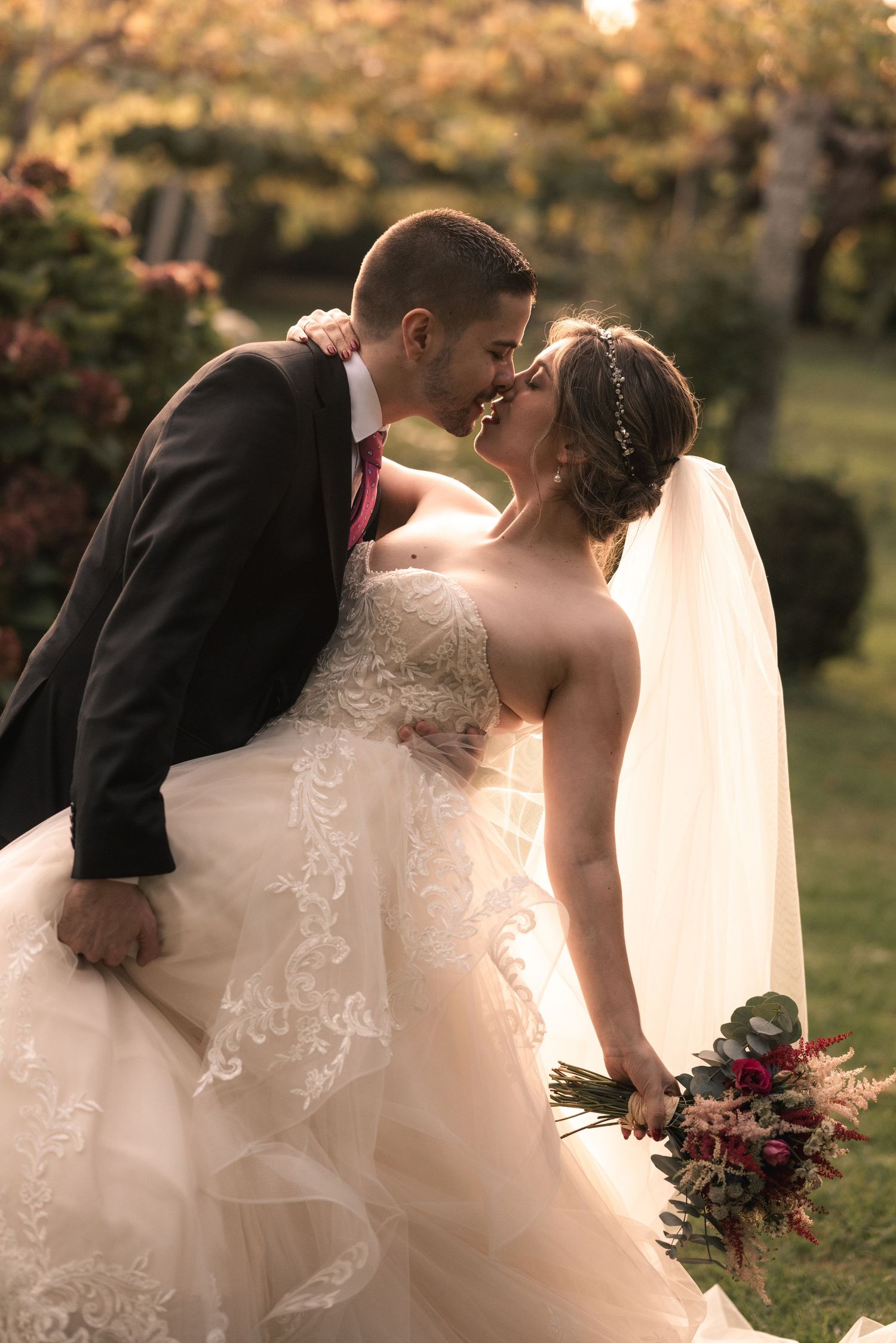 A romantic wedding couple shares intimate kisses in a garden setting during golden hour.