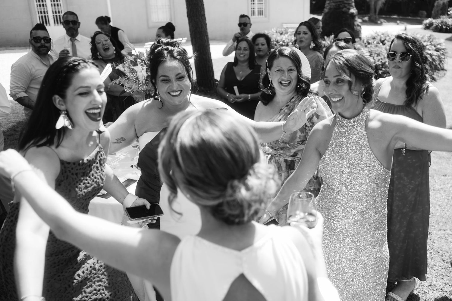 Wedding celebration with guests dancing and laughing together outdoors.