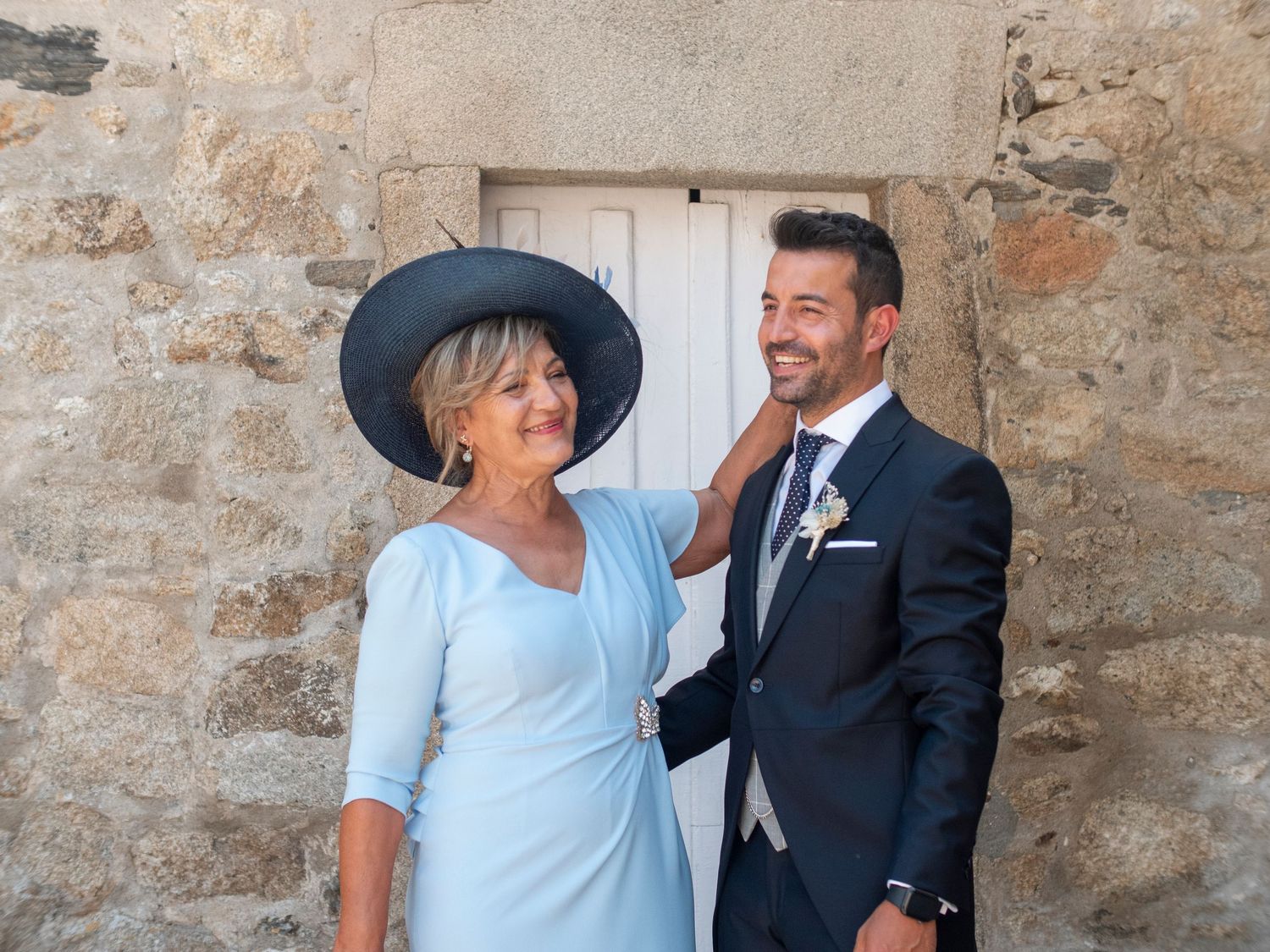 Stone wall backdrop with figures in formal attire including a light blue dress and dark suit.
