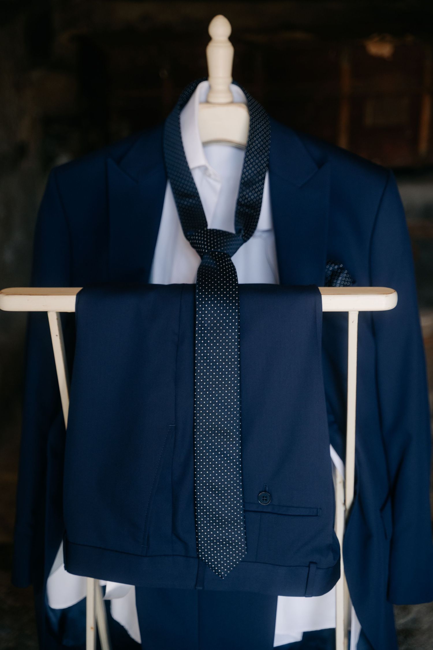 A navy blue suit jacket with white dress shirt and polka dot tie displayed on a mannequin in different angles.