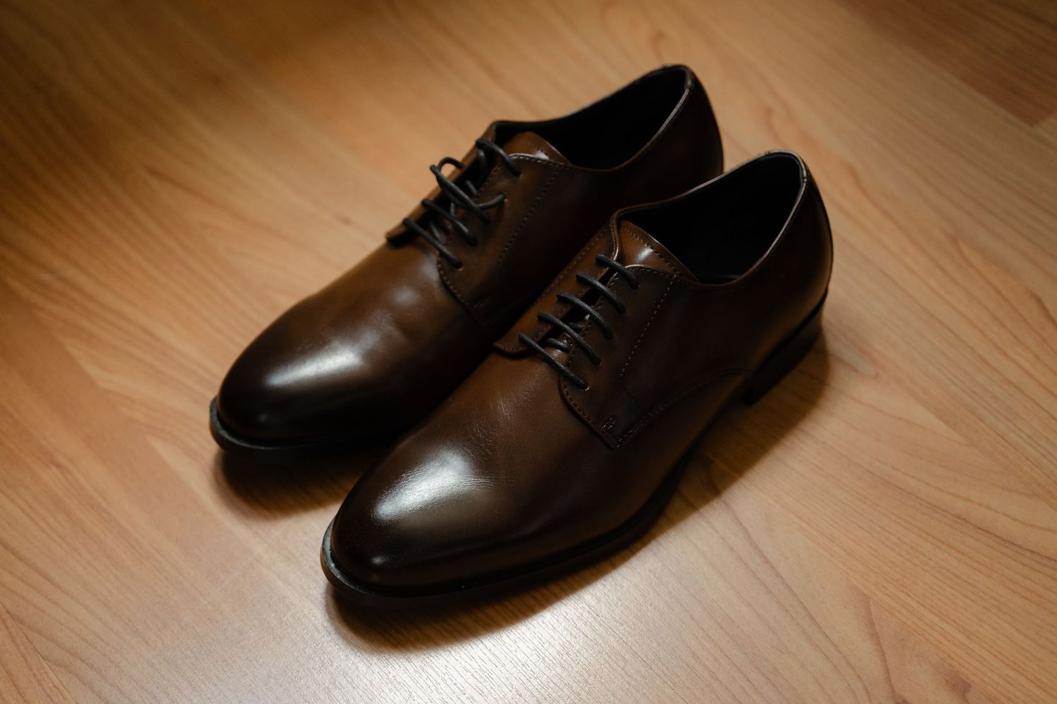 A pair of classic brown leather oxford dress shoes shown from different angles on a wooden floor.