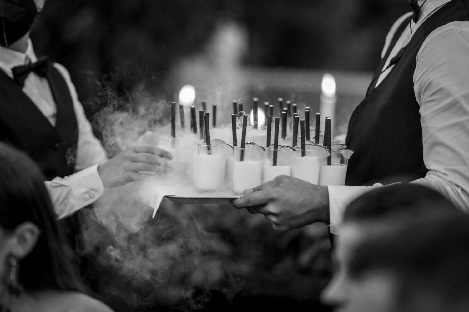 Black and white photo of candles and smoke on a table being served at an elegant event.