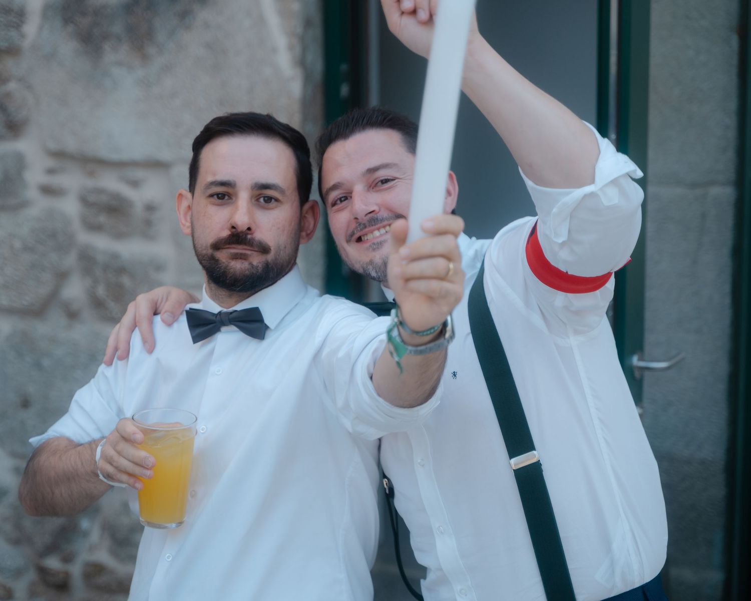 Groomsmen in white shirts and suspenders raise drinks for a celebratory toast.