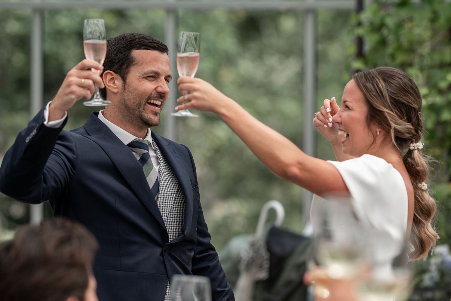 A bride and groom share a joyful moment while raising champagne glasses in a toast during their wedding celebration.