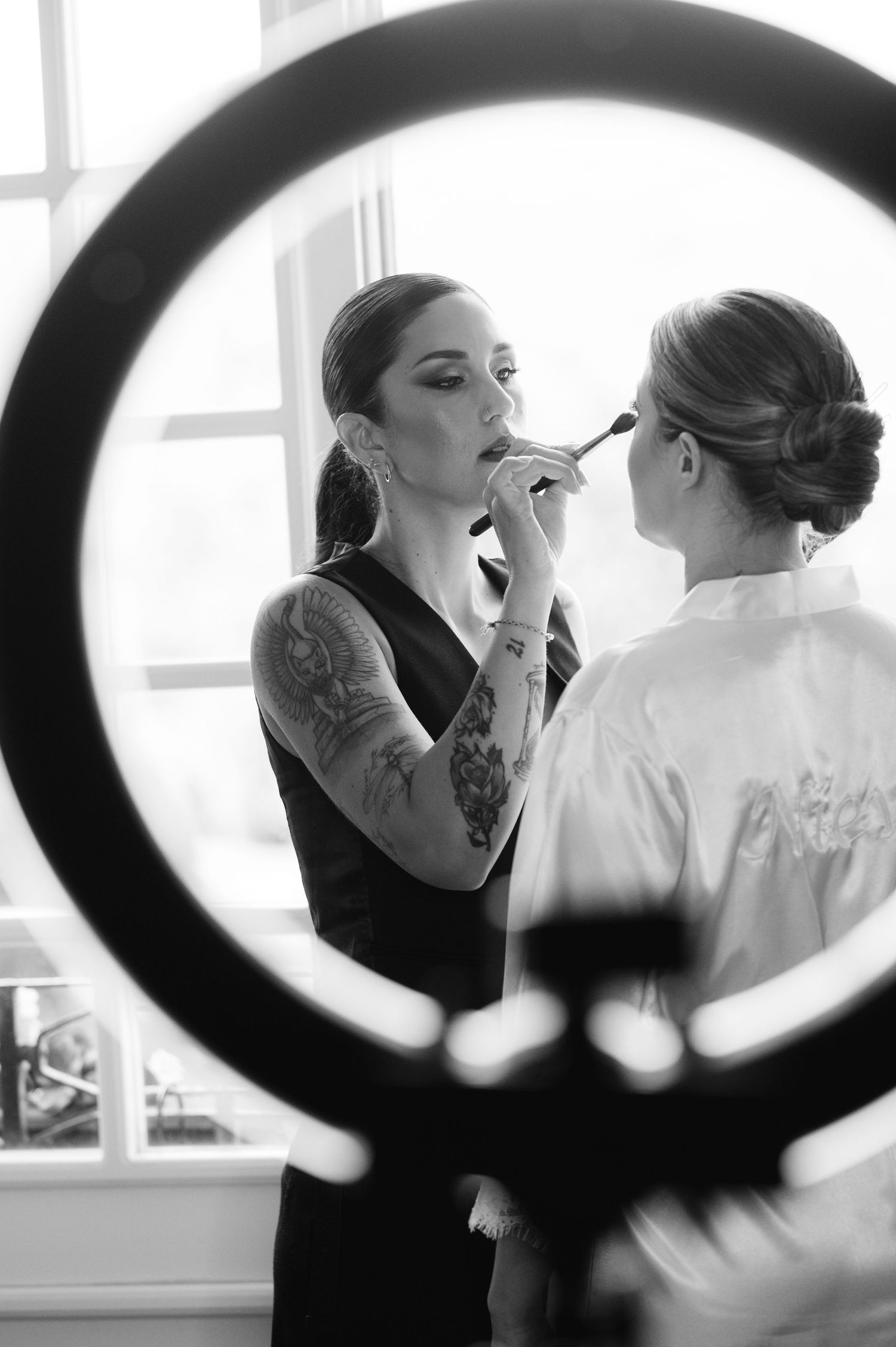Black and white image of makeup application session captured through circular mirror reflection.