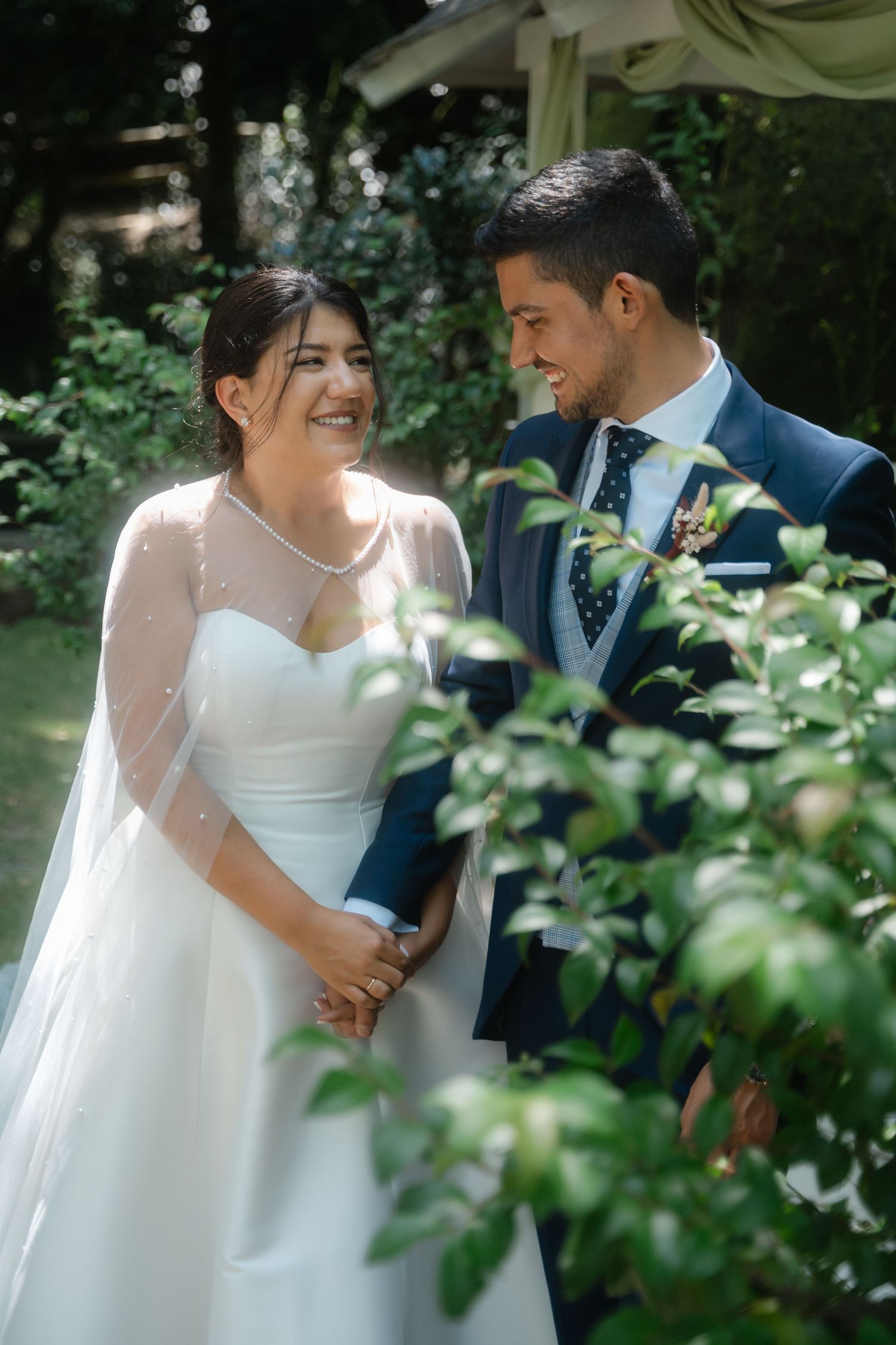 Romantic wedding portraits through foliage showing tender moments between newlyweds in a garden.