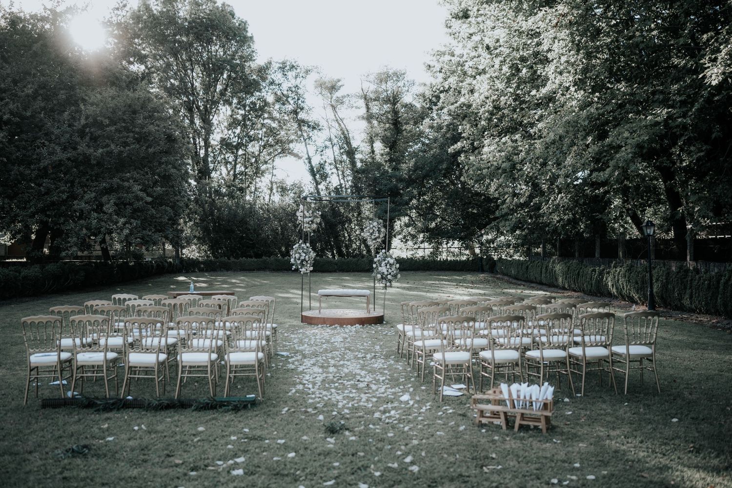 Rows of white chairs arranged outdoors for a garden wedding ceremony with flower petals scattered on the grass.