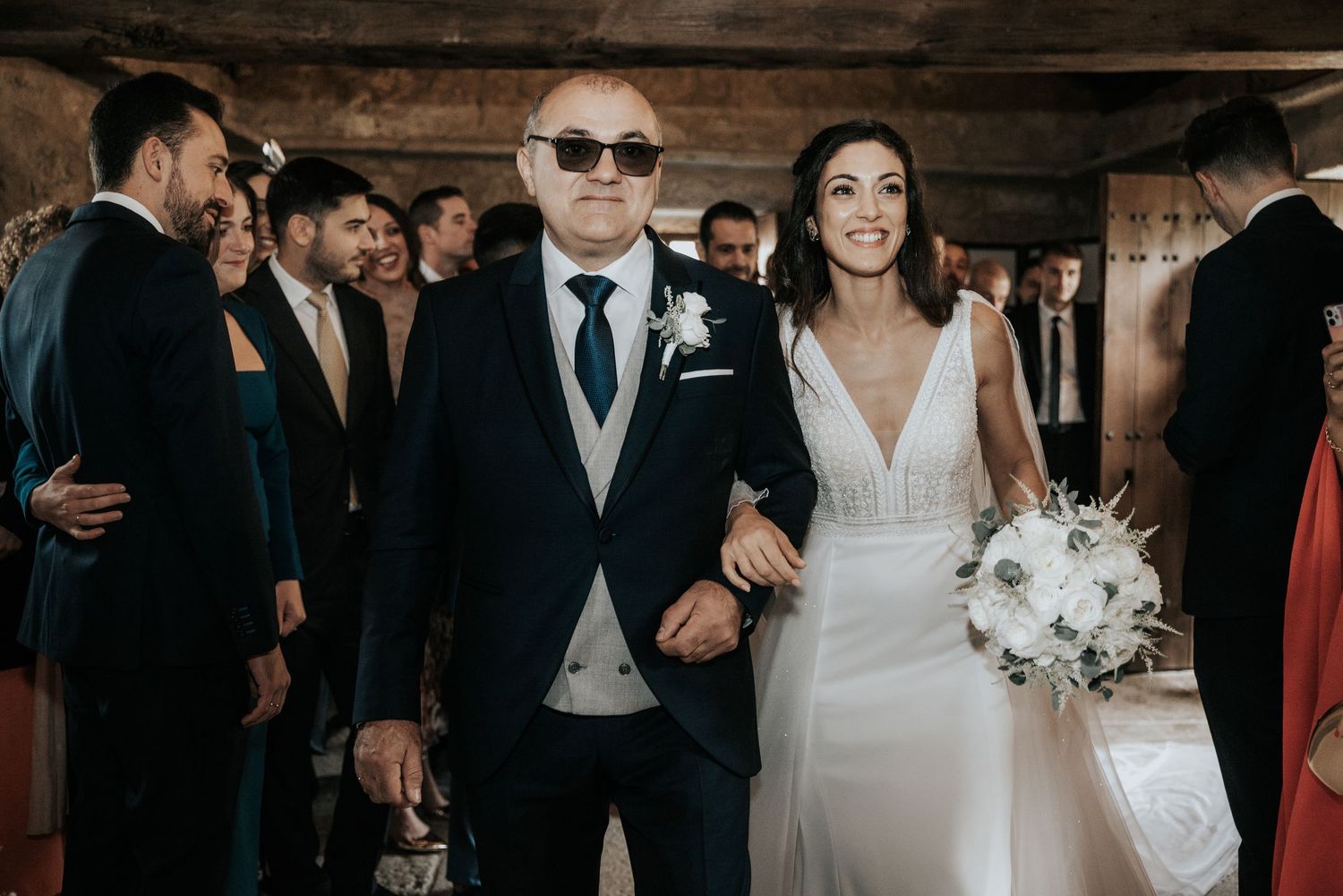 Wedding party celebrates during reception with guests dancing and mingling in an indoor venue.