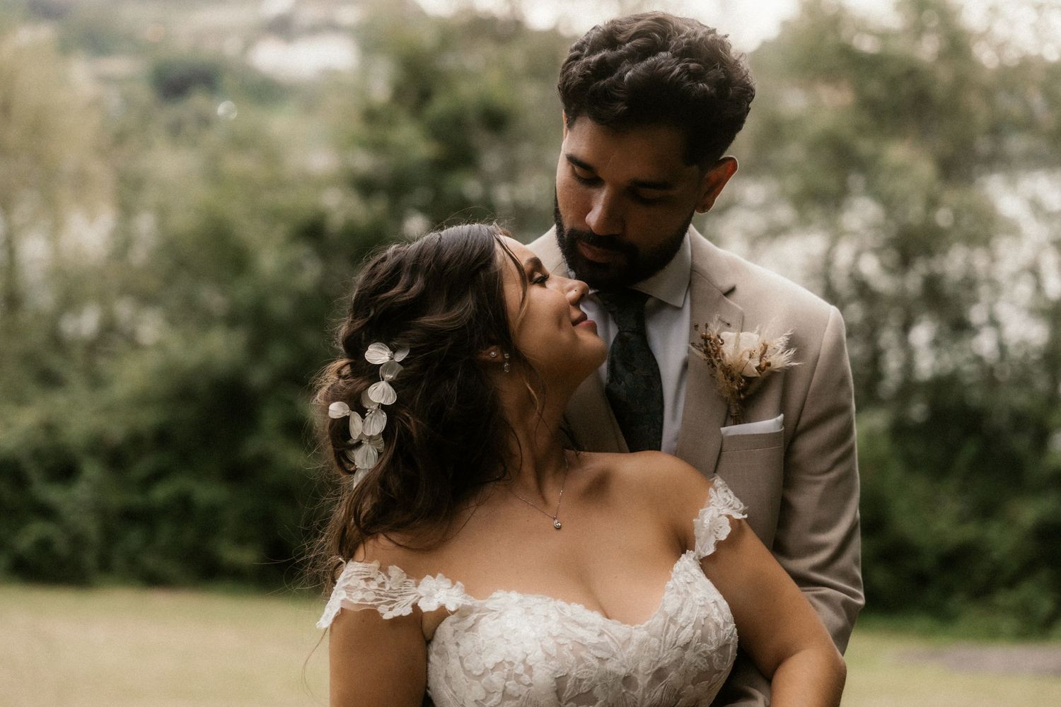 A romantic couple in wedding attire embraces outdoors in a natural setting during golden hour.