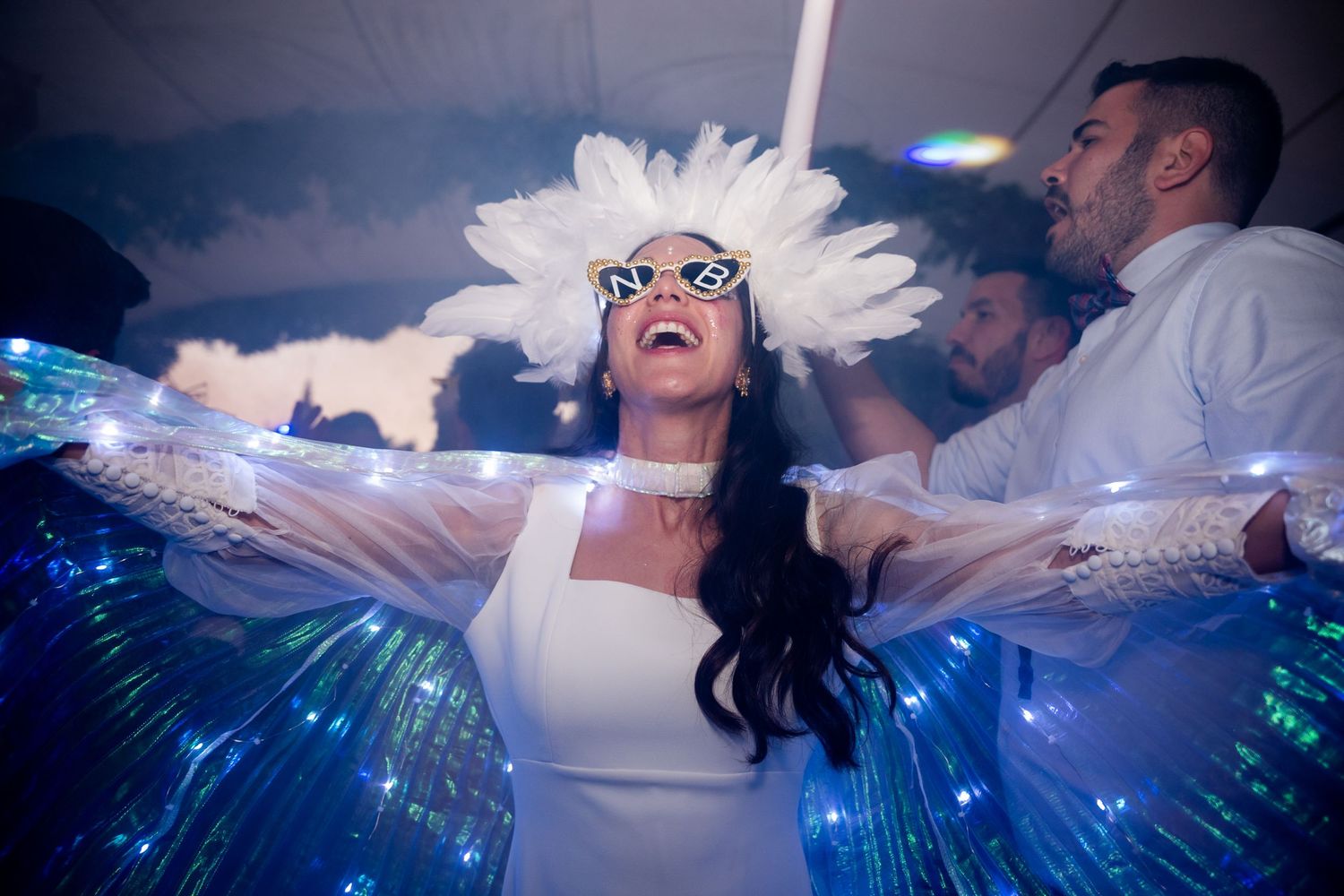 Wedding guests dance and celebrate on a dark dance floor illuminated by blue lights and special effects.