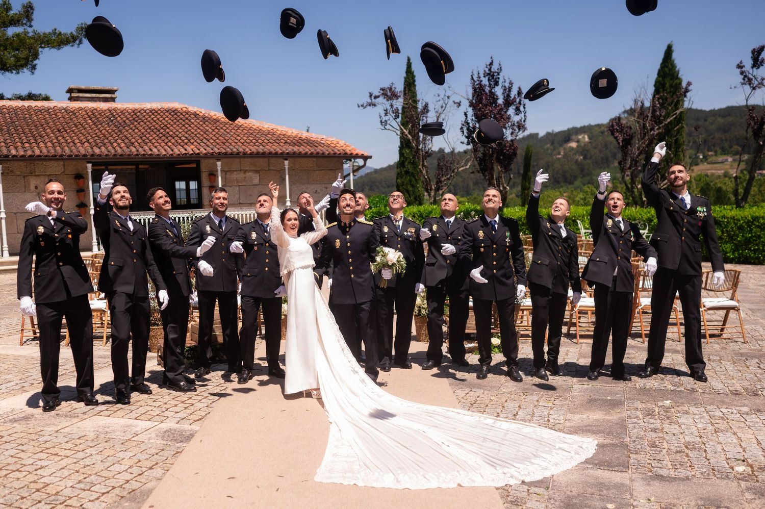 Military officers throw their caps in celebration during a wedding photo on a terrace.