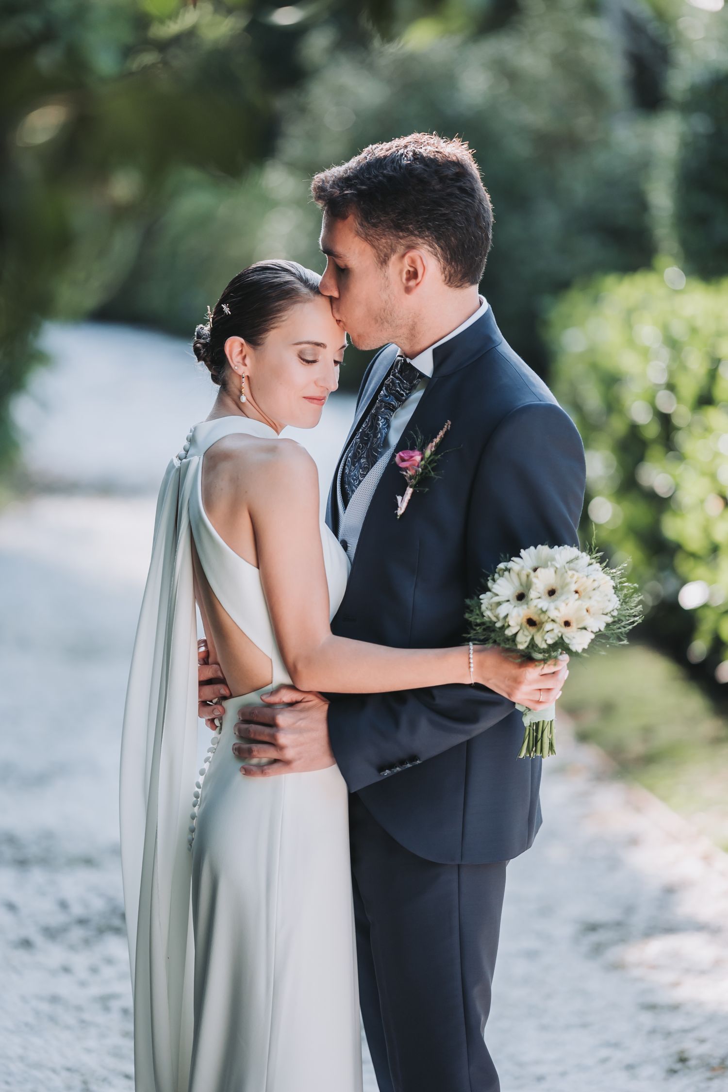 A romantic wedding couple shares intimate moments in a garden setting with white flowers and flowing veil.