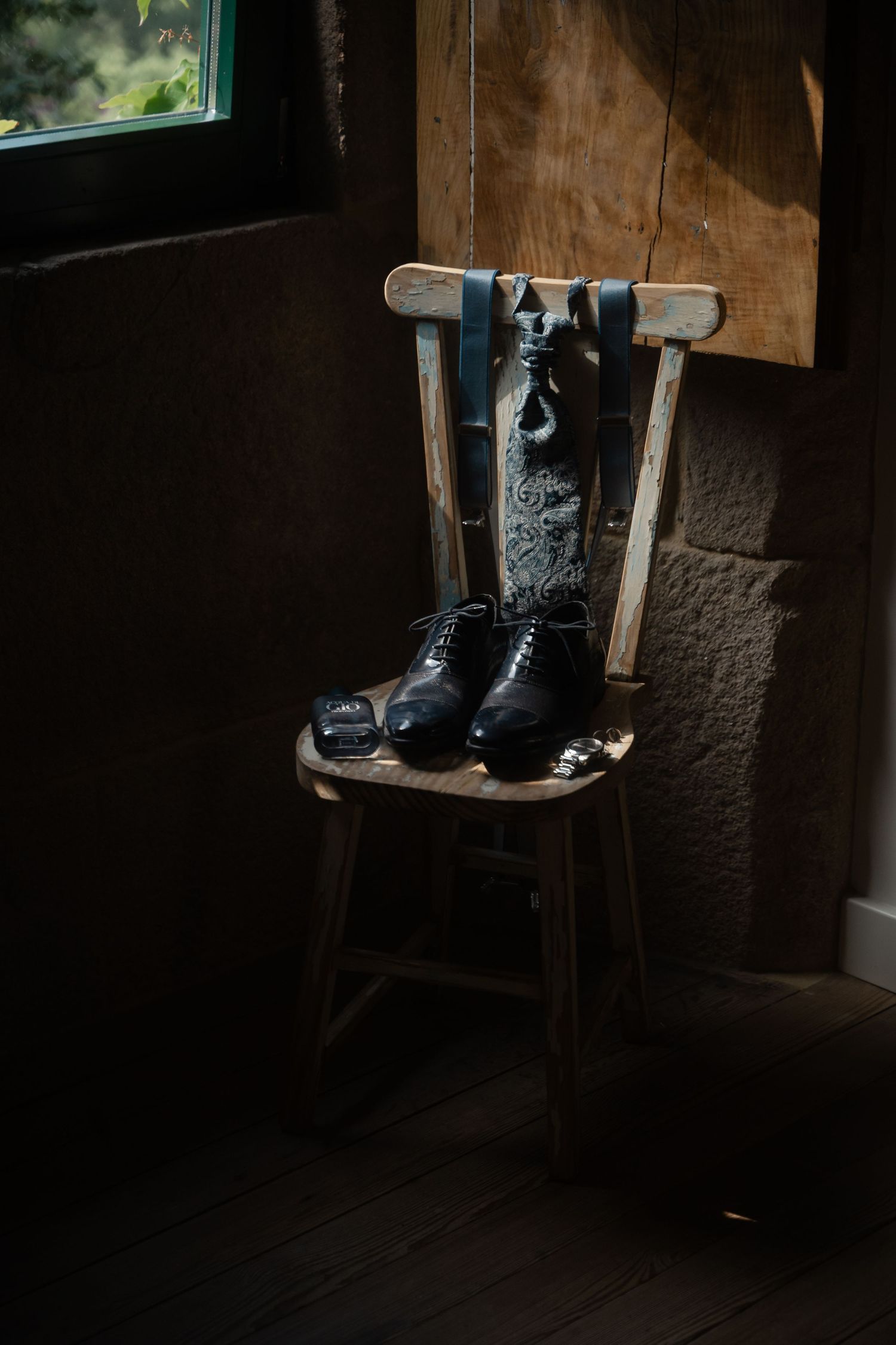 A dark moody still life photograph of vintage boots displayed on a wooden shelf in a dimly lit rustic interior.