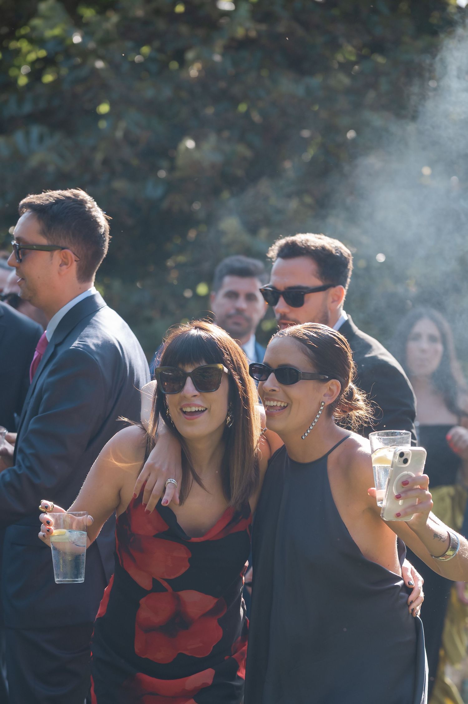 Wedding guests enjoying an outdoor reception with laughter and sunglasses.