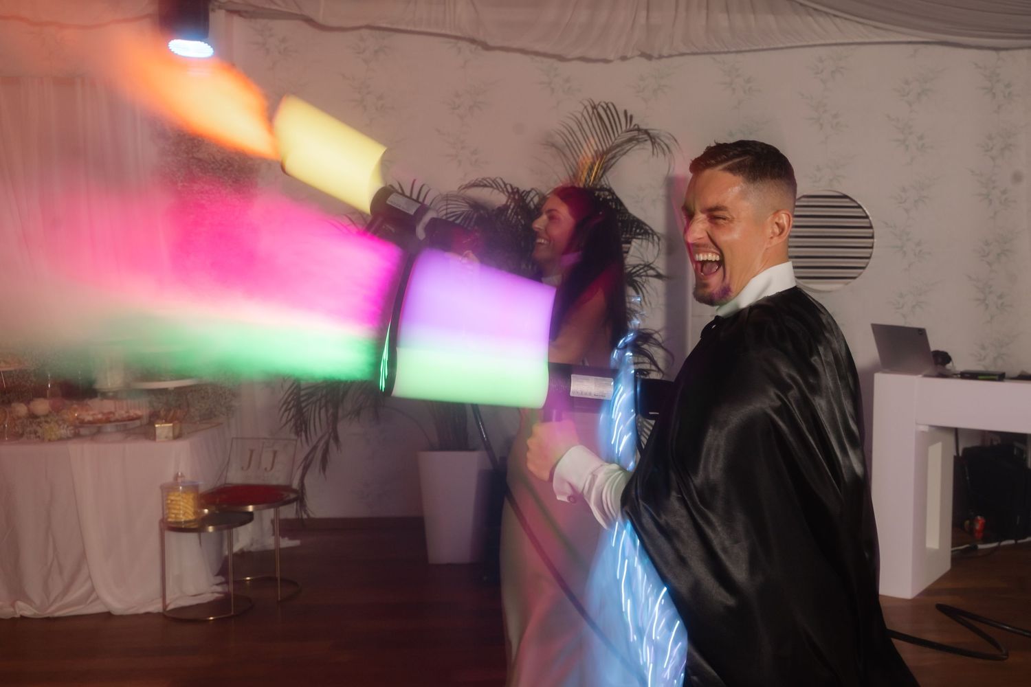 A performer creates colorful light effects with handheld devices at an indoor party.