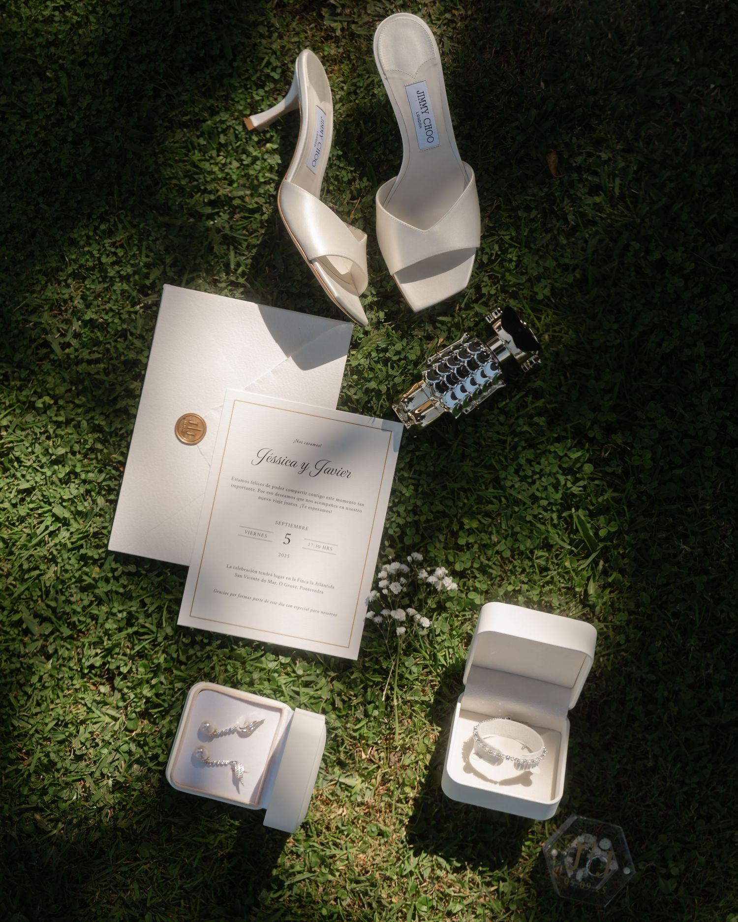 Wedding accessories including invitation, shoes and jewelry arranged on grass in dramatic lighting.