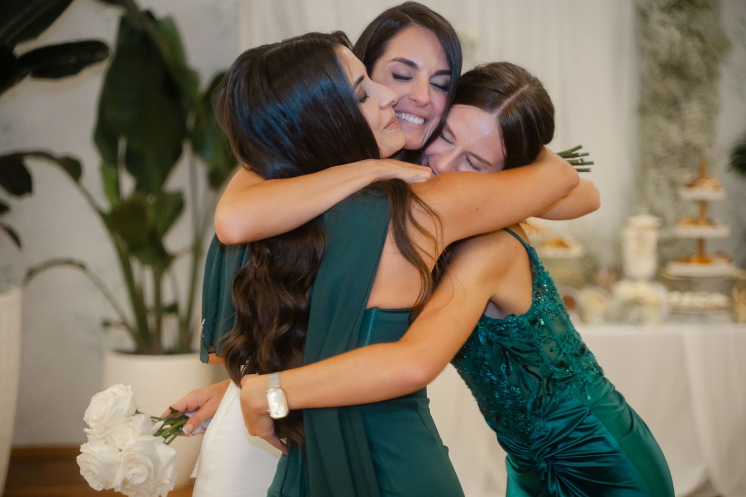 Two people in emerald green dresses embrace warmly during a special celebration.