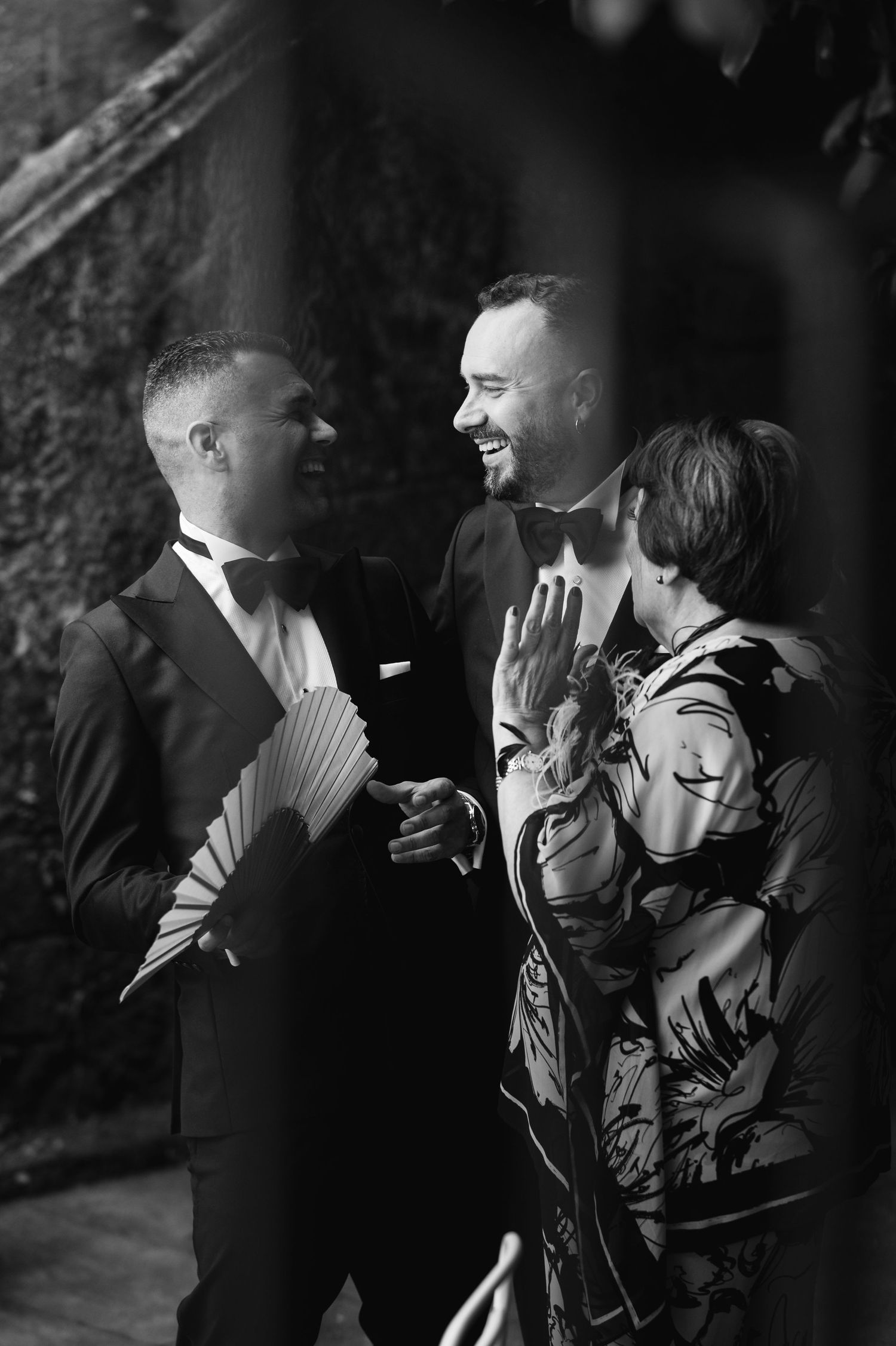 A candid black and white moment of three people laughing and sharing a joyful conversation at a formal event.