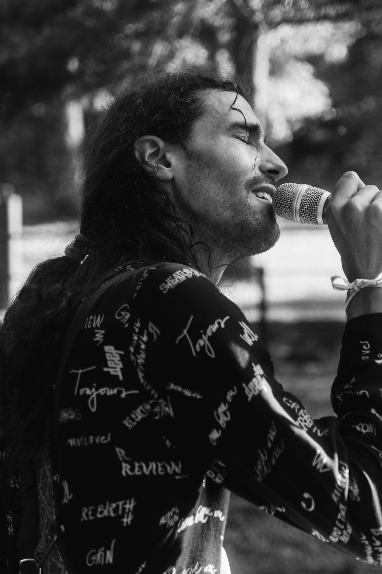 Black and white portrait of a performer singing into a microphone wearing a patterned jacket.