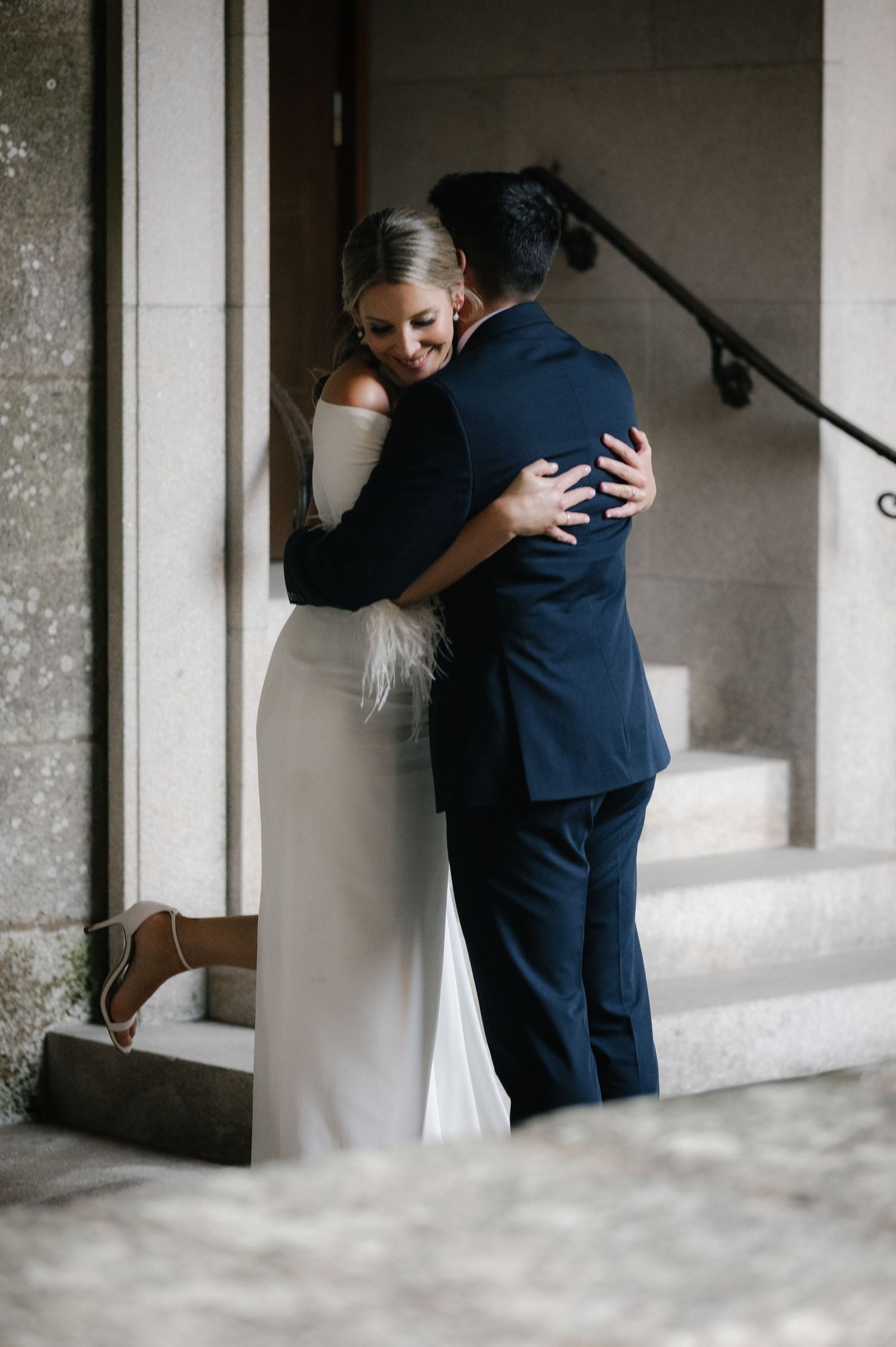 Intimate wedding embrace captured in minimalist architectural setting with soft lighting.