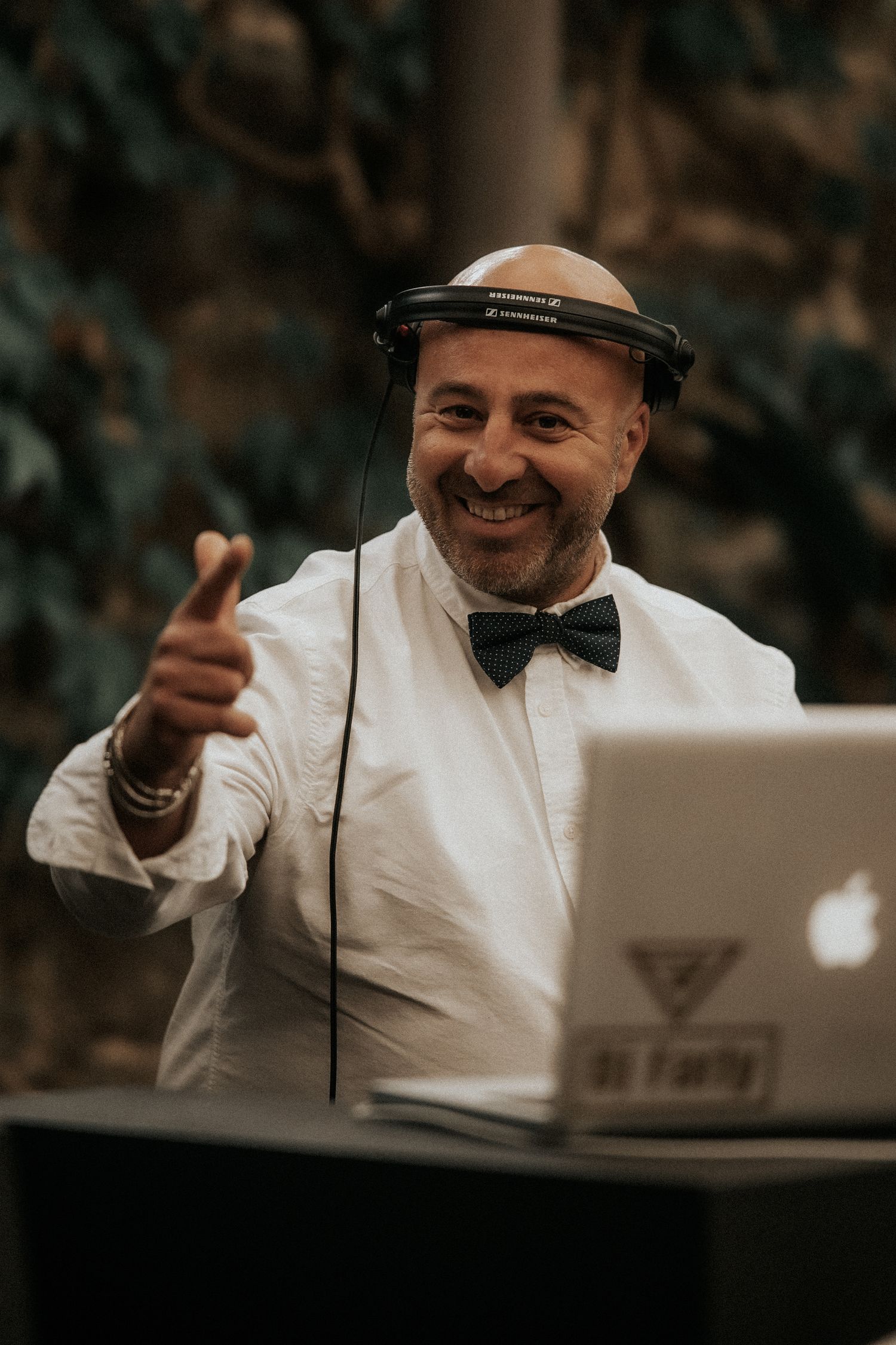 DJ in white dress shirt and bow tie smiles while performing at an event with professional equipment.
