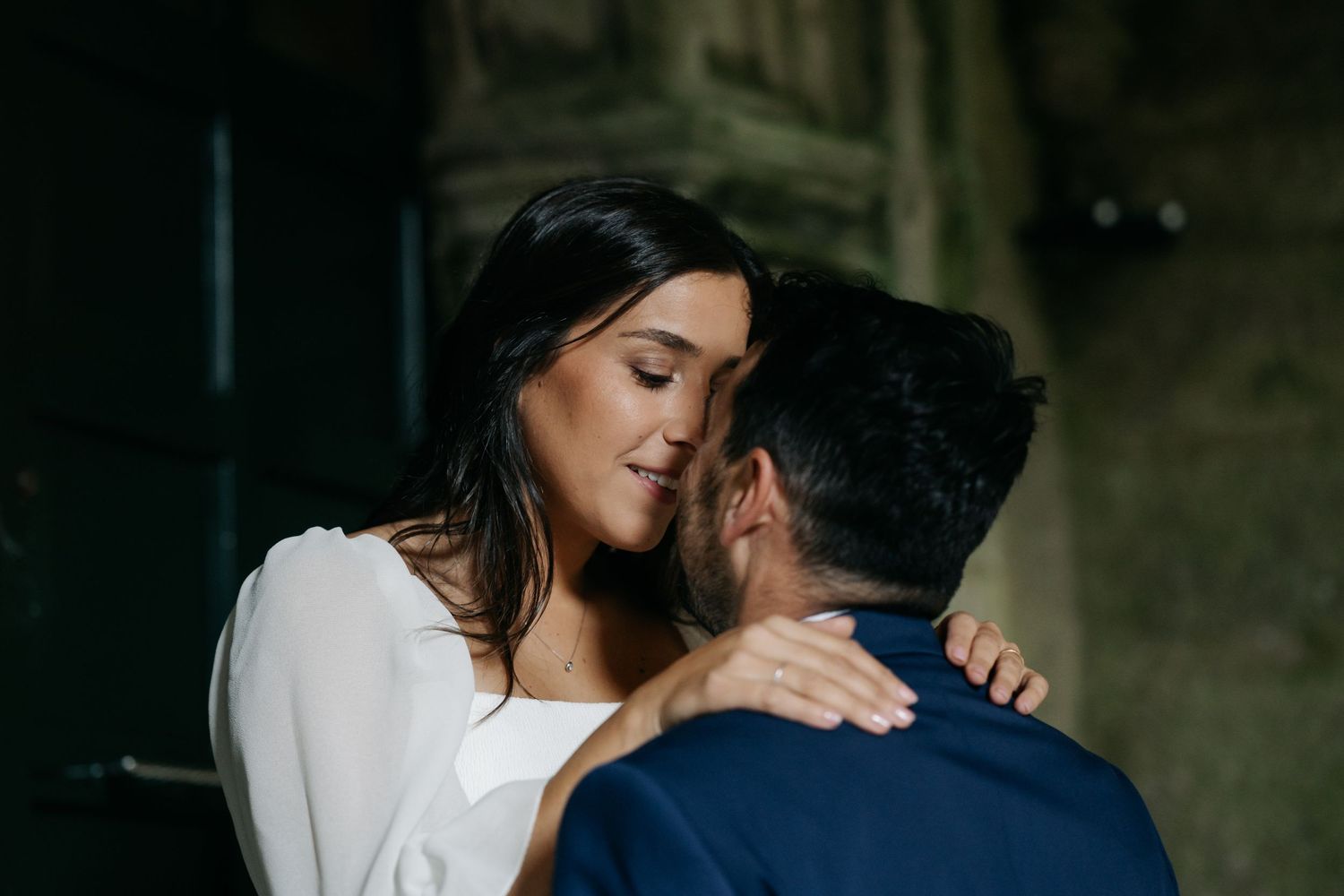 A romantic couple embraces in a dimly lit setting wearing white and dark clothing.