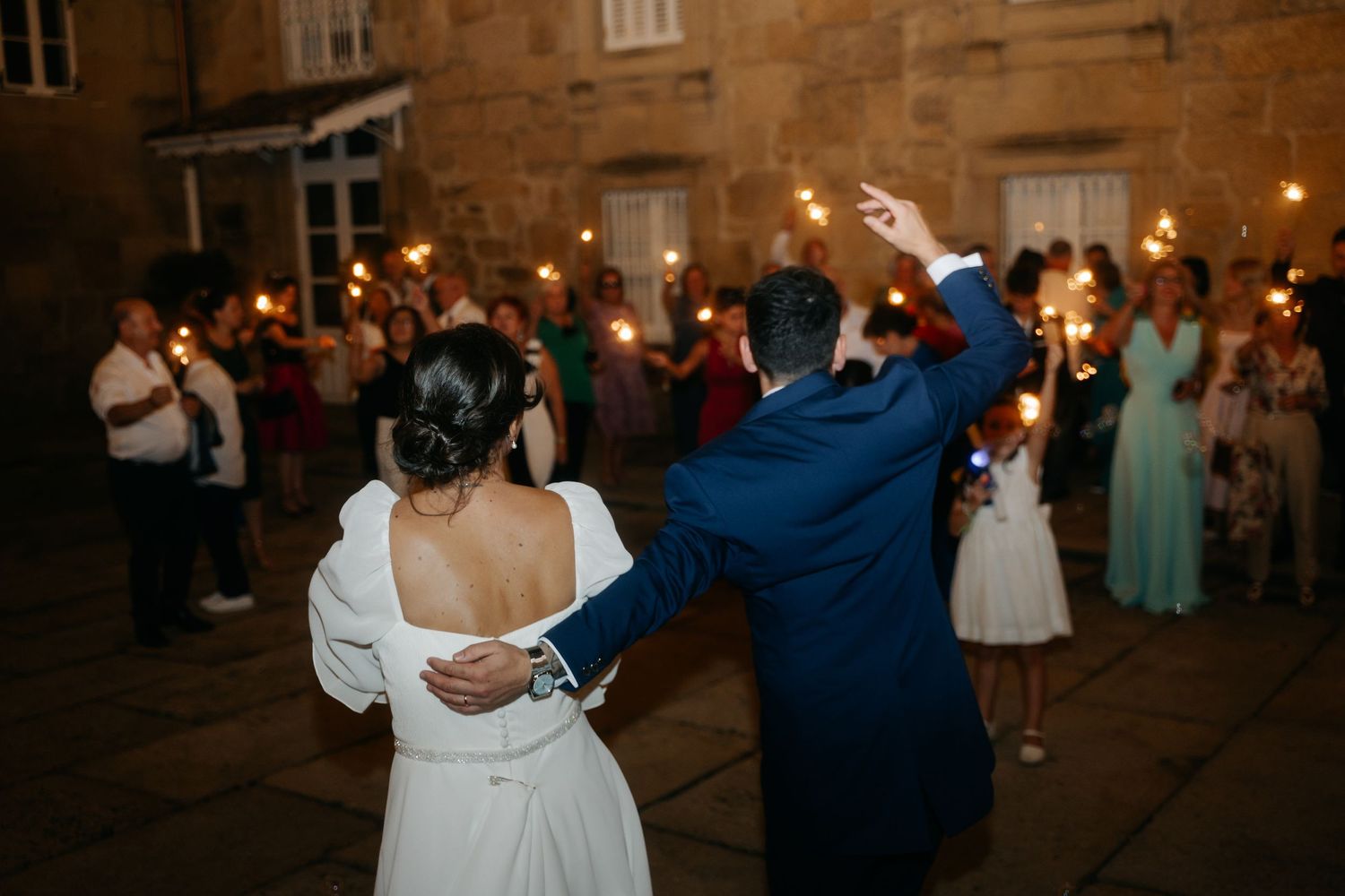 A couple dances together during a romantic evening celebration with sparklers held by guests in the background.