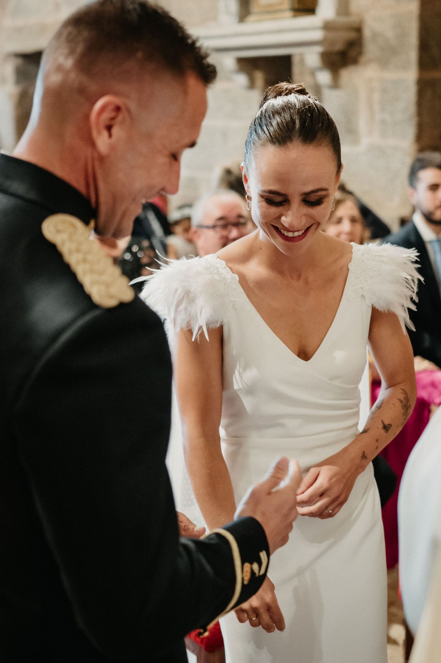 Bride in white dress with feather details smiling during wedding ceremony.