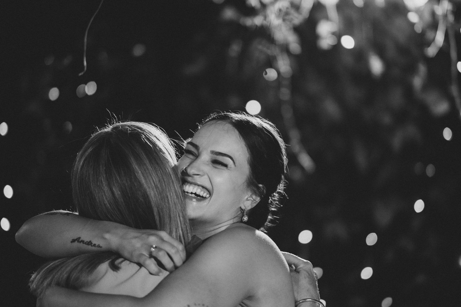 A joyful black and white moment captured during an embrace with twinkling lights in the background.