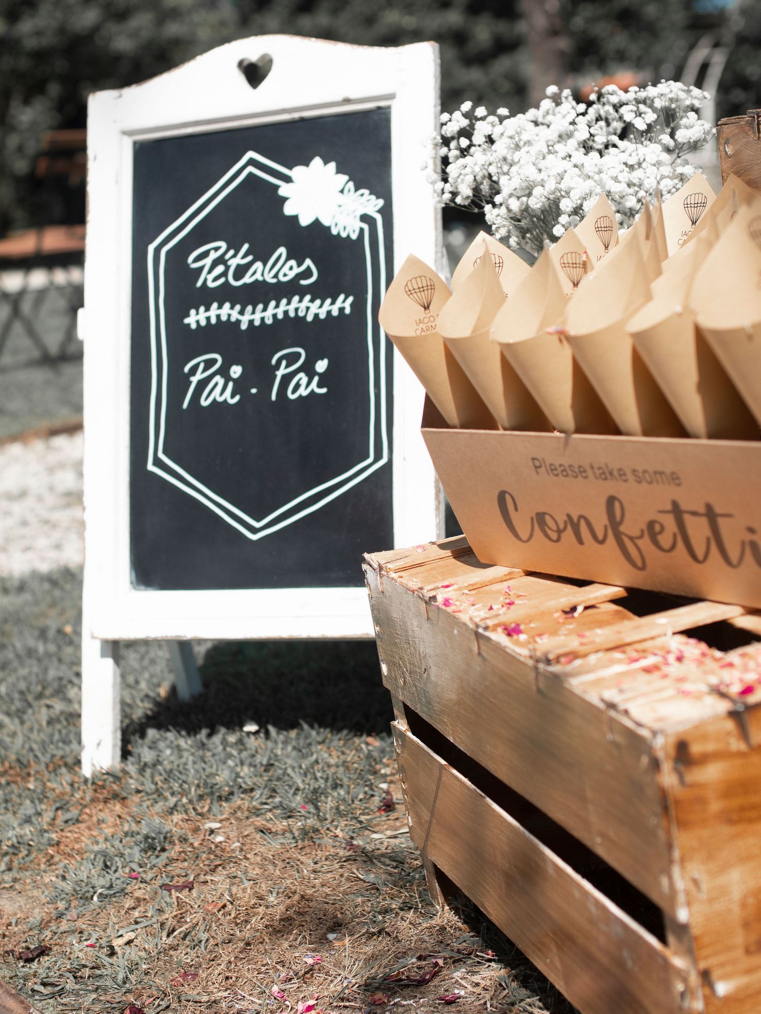 Rustic wooden boxes with chalkboard signs displaying wedding favors and confetti at an outdoor celebration setup.